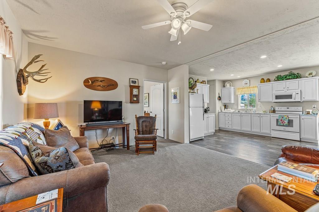 Living area featuring a textured ceiling, ceiling fan, dark colored carpet, and recessed lighting
