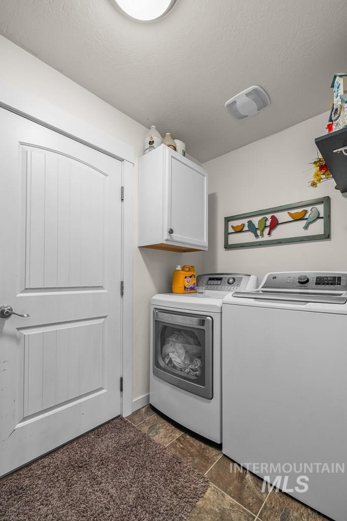 Laundry area with a textured ceiling, washing machine and dryer, dark stone finish floors, and cabinet space