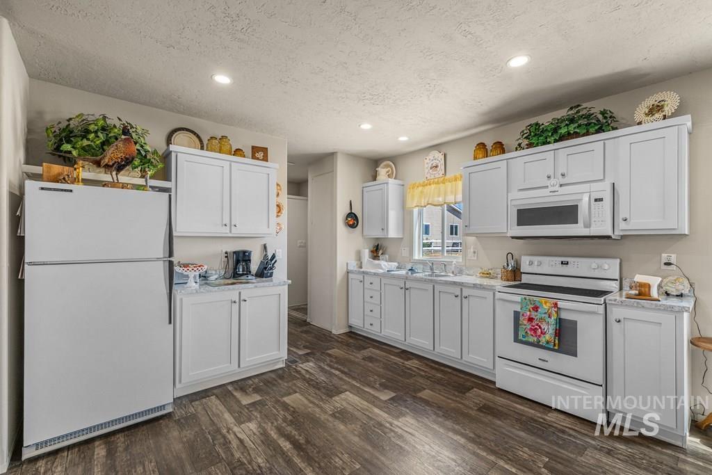 Kitchen featuring white appliances, dark wood-style flooring, a textured ceiling, recessed lighting, and white cabinets