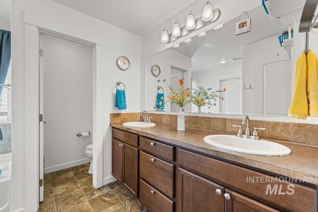 Full bath featuring double vanity, stone finish floors, and a tub to relax in
