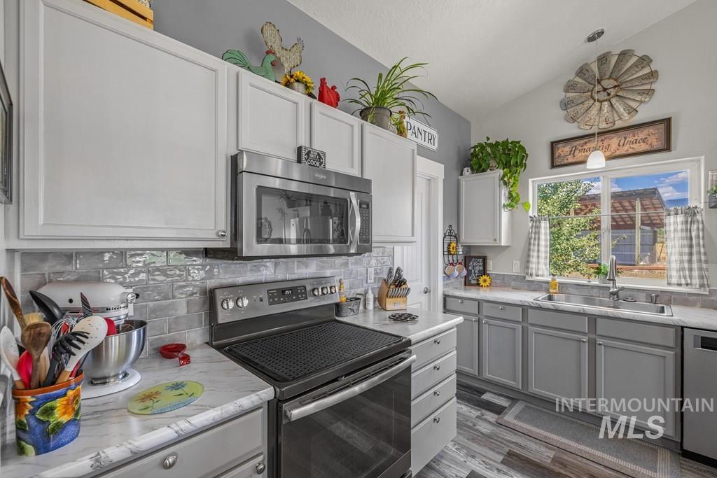 Kitchen with stainless steel appliances, light countertops, backsplash, lofted ceiling, and dark wood-style floors