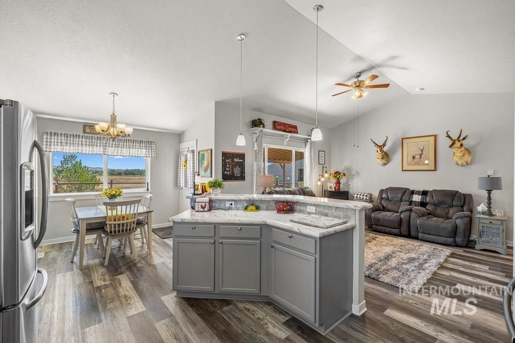 Kitchen with lofted ceiling, gray cabinetry, stainless steel refrigerator with ice dispenser, hanging light fixtures, and dark wood finished floors