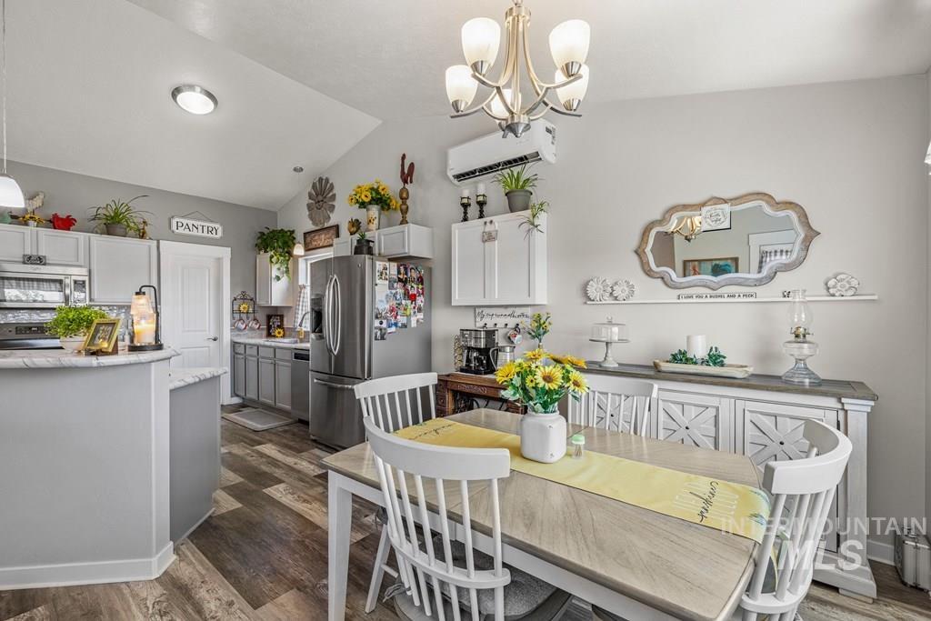 Dining area with lofted ceiling, dark wood-style flooring, a chandelier, and an AC wall unit