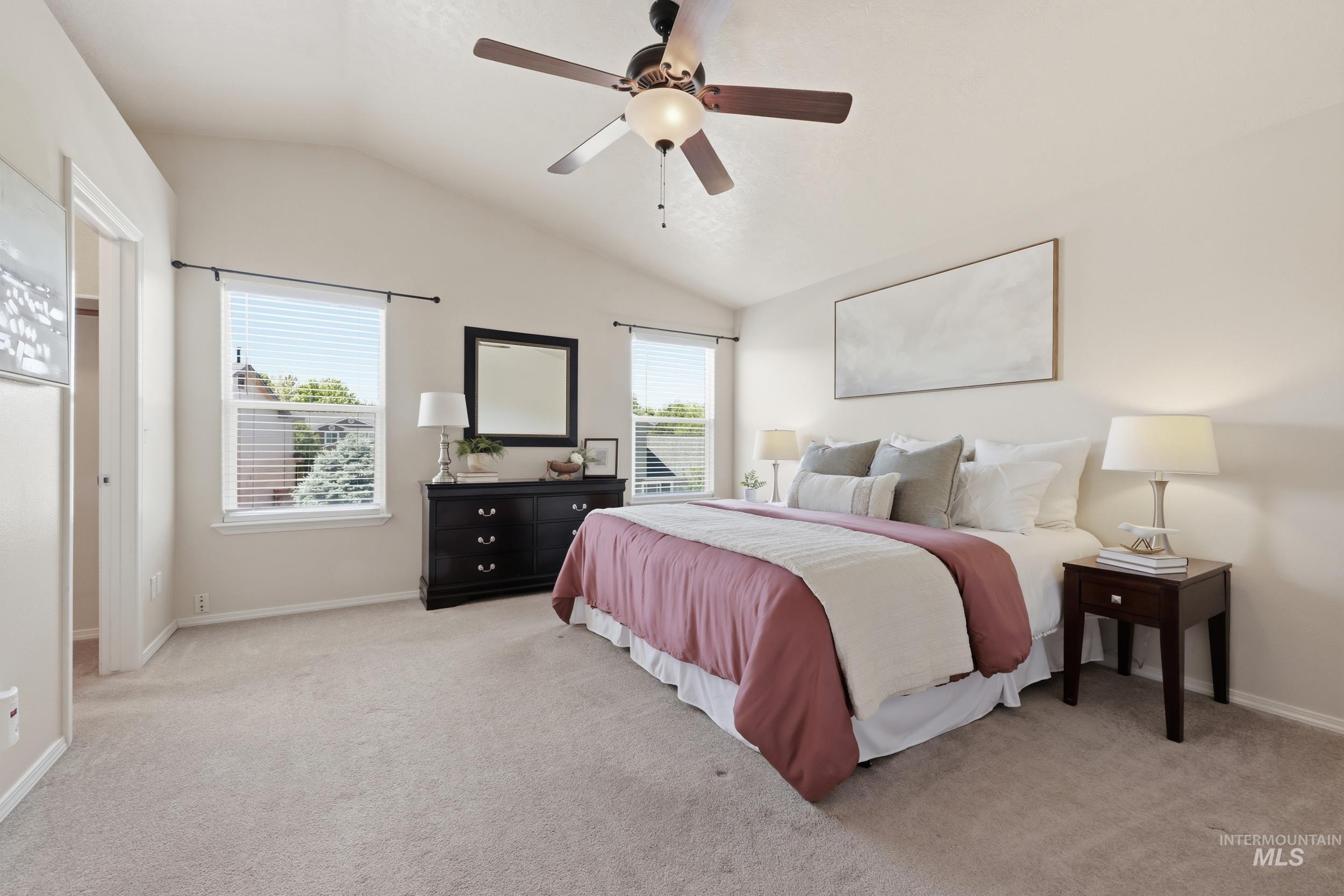 Vaulted ceiling bedroom with a ceiling fan, light-toned carpeting, and two double-hung windows