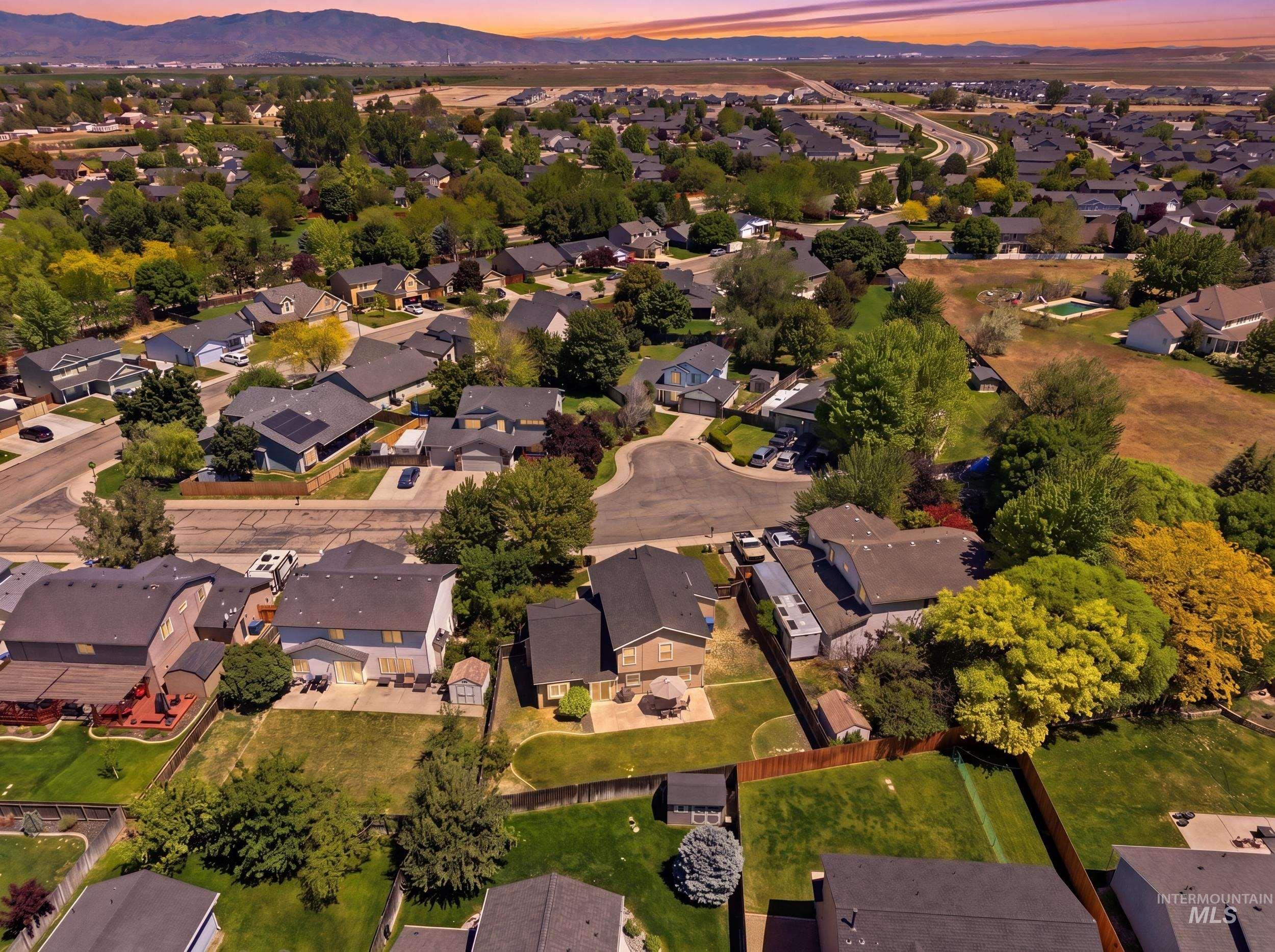 Aerial perspective of a residential community featuring established homes, mature trees, and mountainous terrain in the background