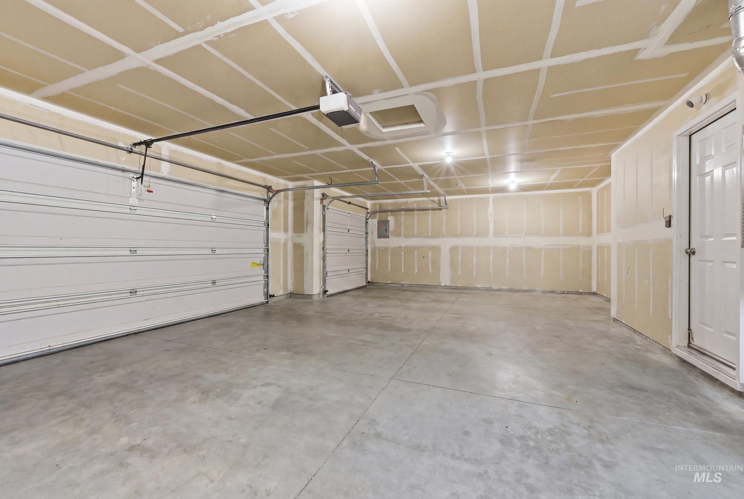 Spacious garage featuring a concrete floor, two white paneled garage doors with automatic openers, and a service entry door