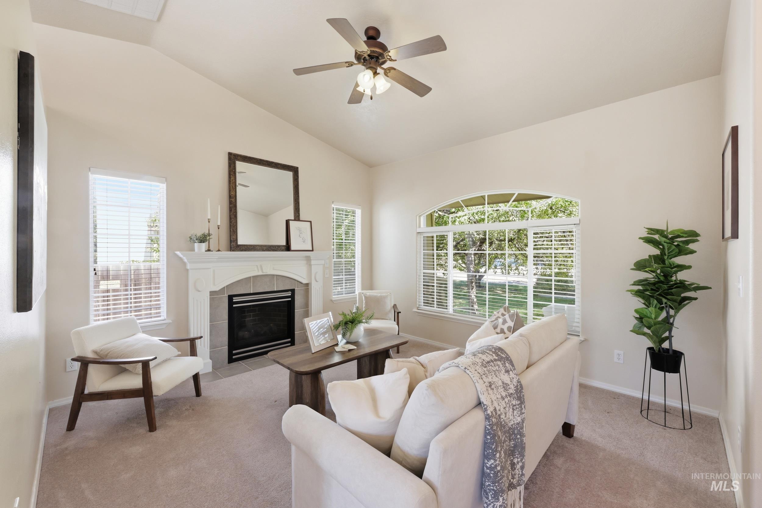 Spacious living area featuring vaulted ceilings, a fireplace with a decorative mantelpiece and tile surround, and an arched window