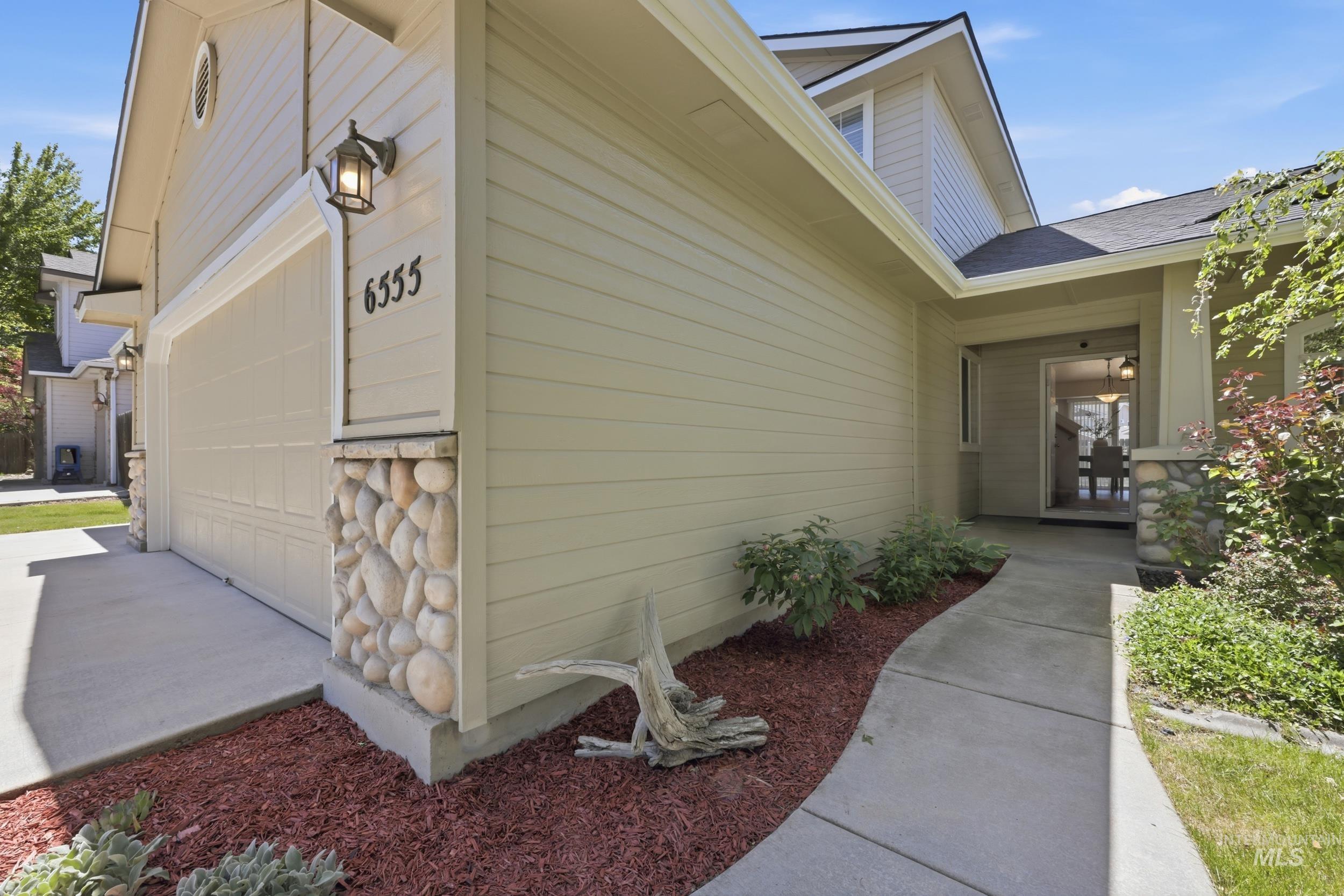 Exterior featuring siding, stone accents, a concrete pathway, and a garage door with integrated lighting