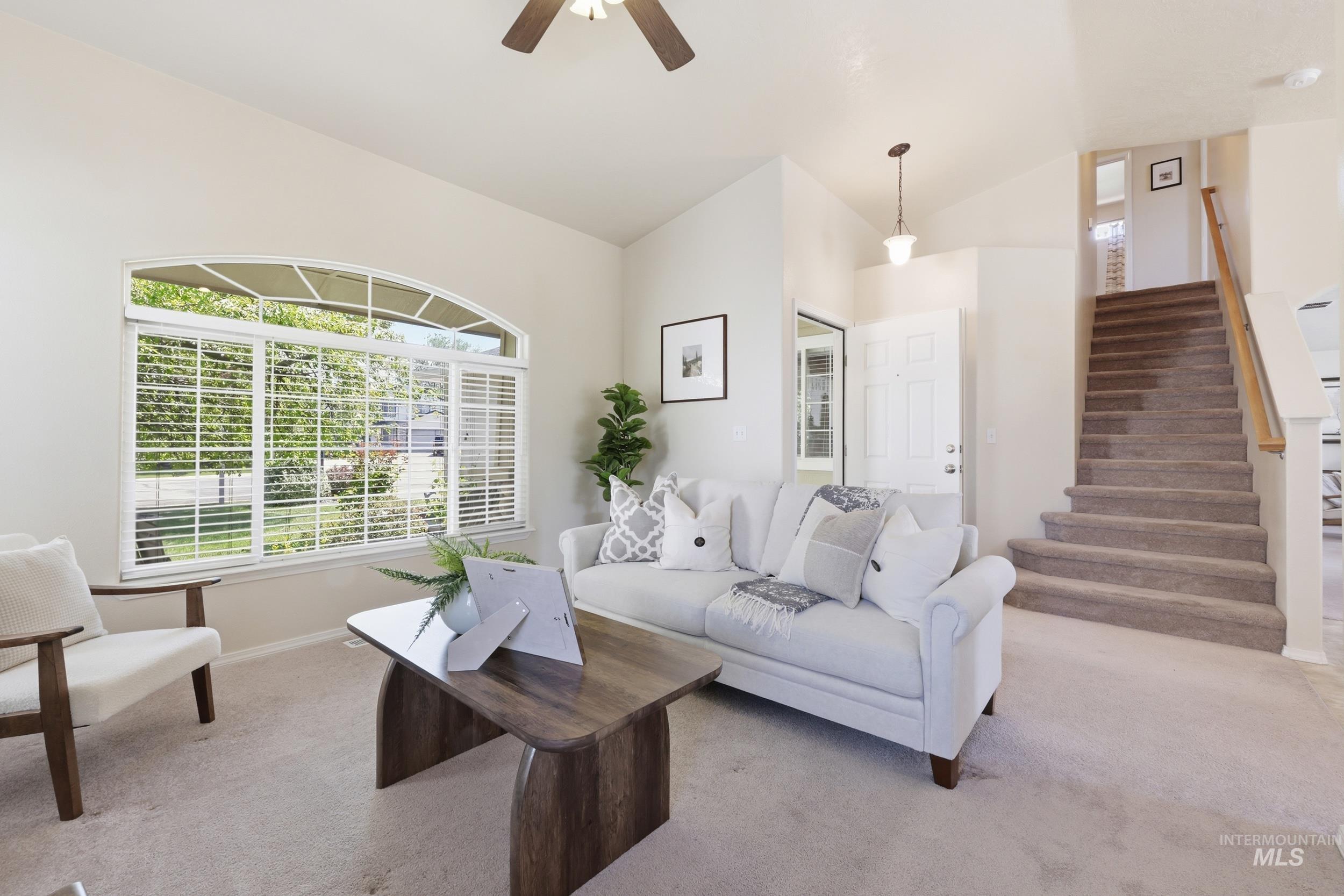 Spacious living area featuring a large arched window with blinds, vaulted ceiling, and carpet flooring