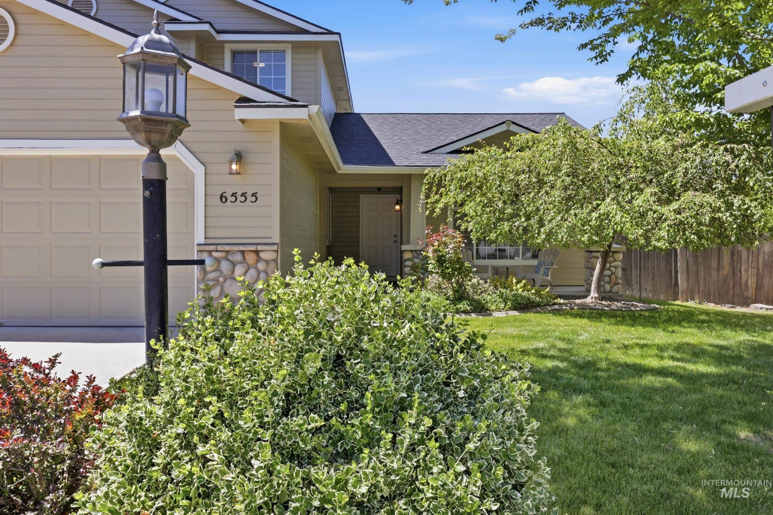 Front exterior featuring horizontal siding, a stone veneer accent, a traditional garage door, and a mature shade tree
