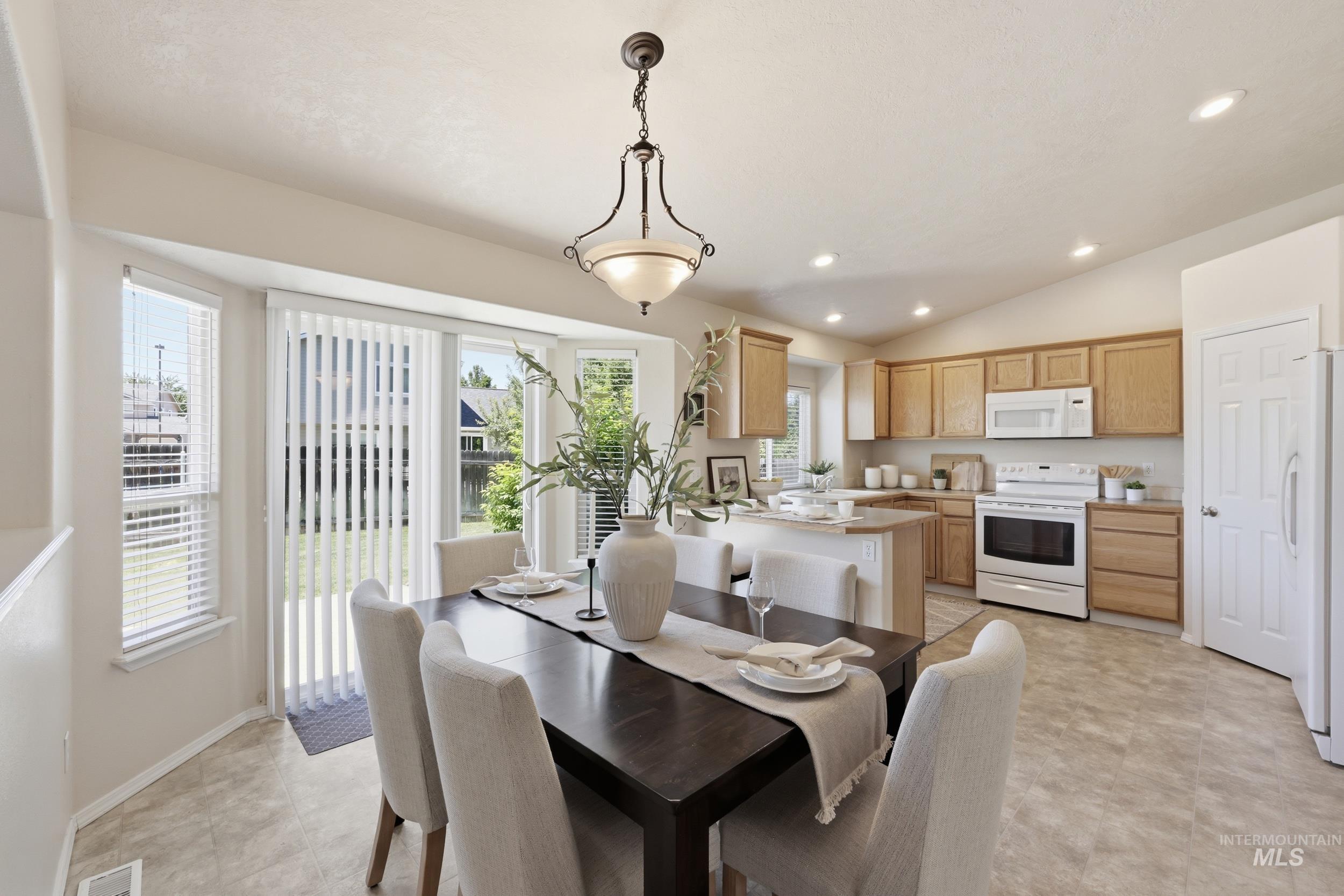 Open-concept kitchen and dining area featuring light wood cabinetry, white appliances, and a central island with bar seating
