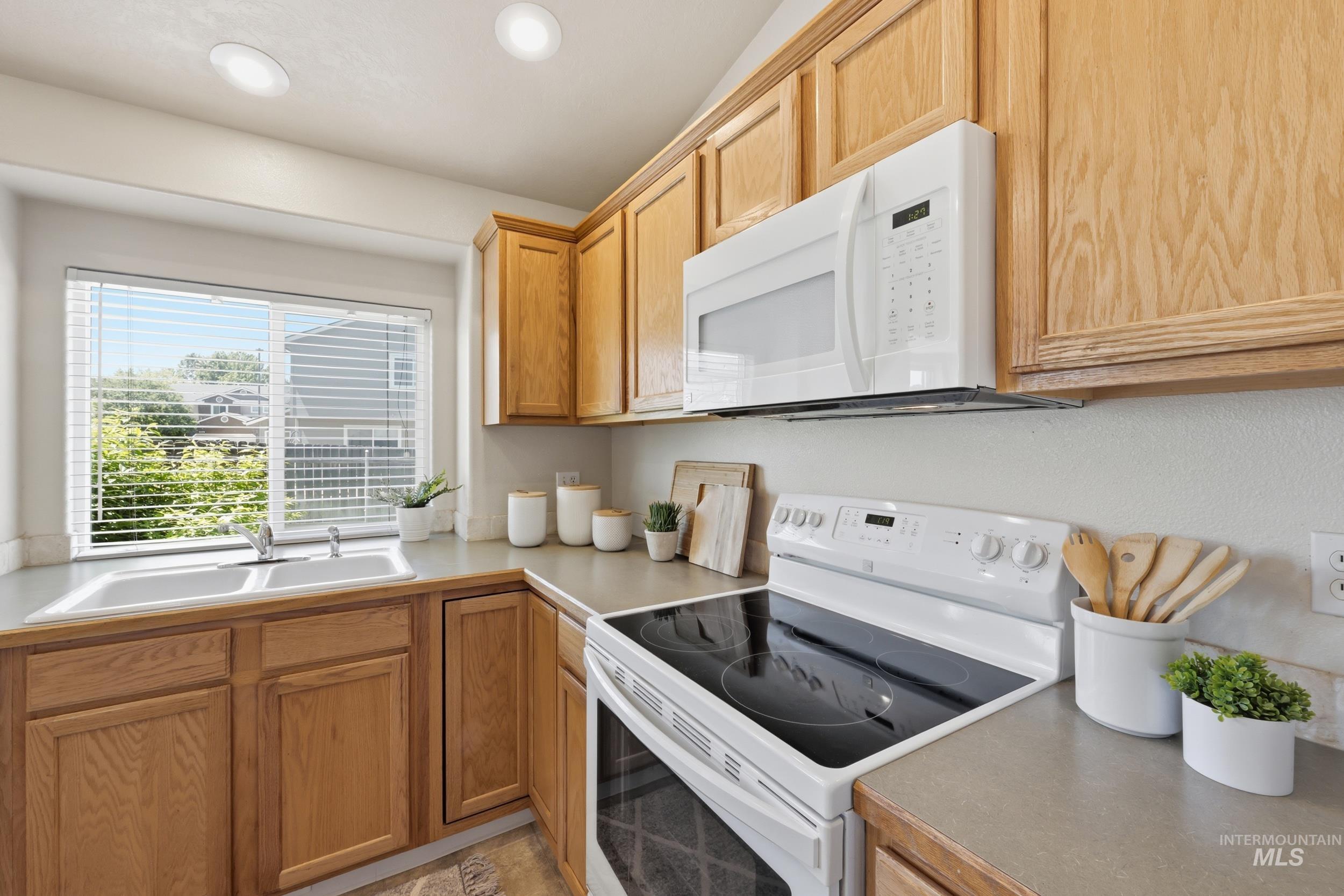 Kitchen featuring wood cabinetry, light countertops, an electric range, an over-the-range microwave, and a double-basin sink under a window