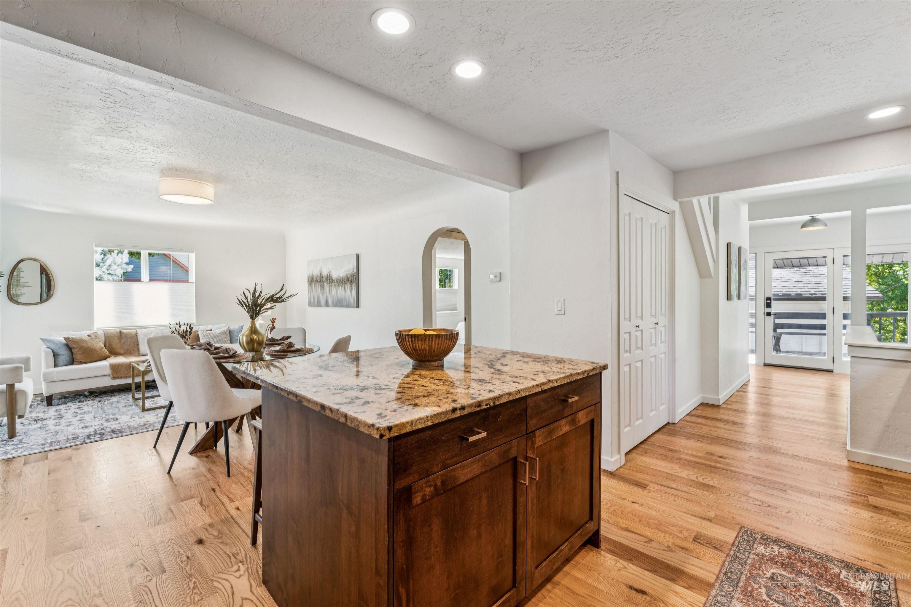 Kitchen featuring a textured ceiling, light stone counters, dark brown cabinetry, open floor plan, and light wood-style floors