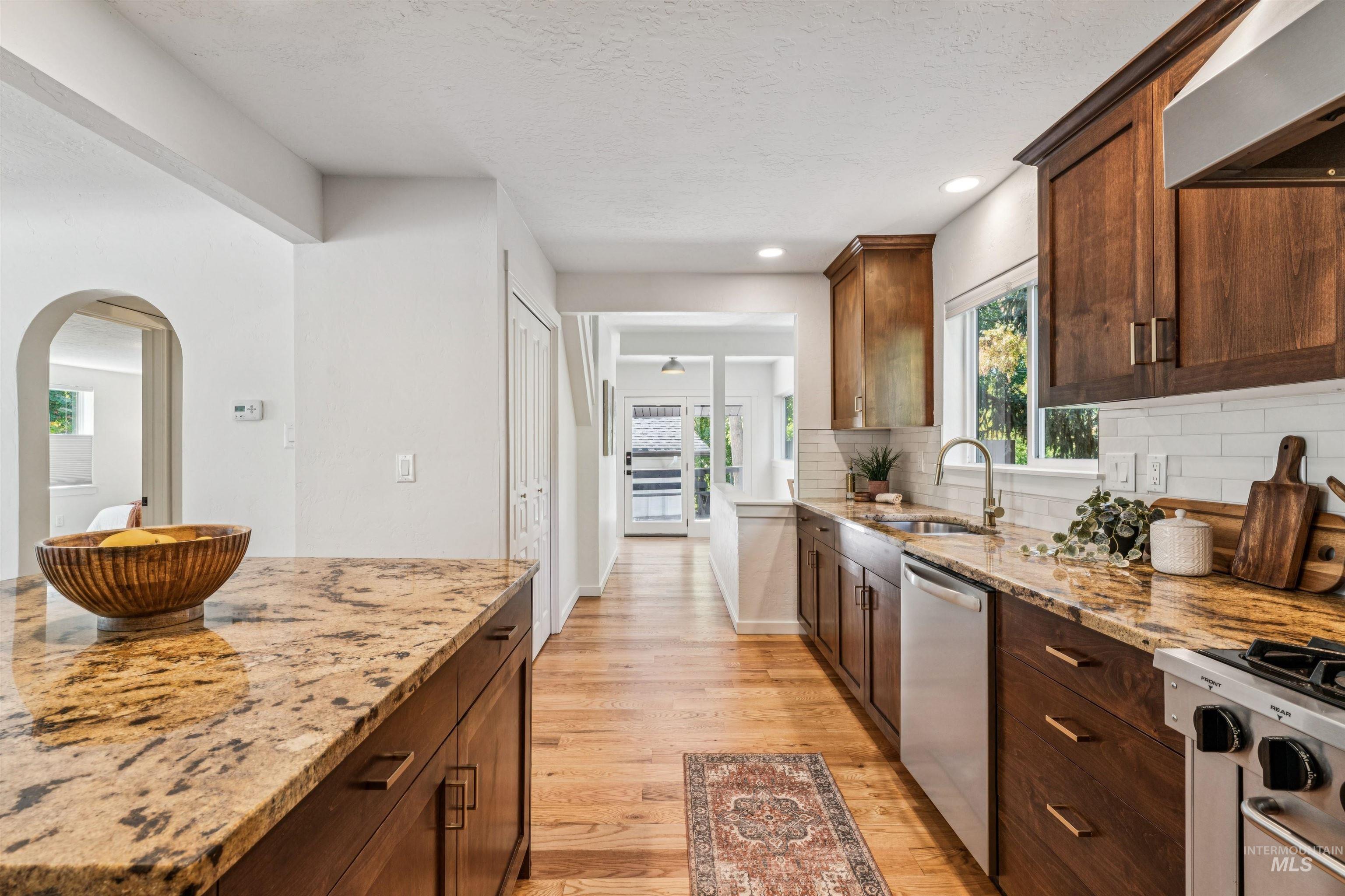 Kitchen featuring light wood finished floors, dark brown cabinets, light stone counters, exhaust hood, and a textured ceiling
