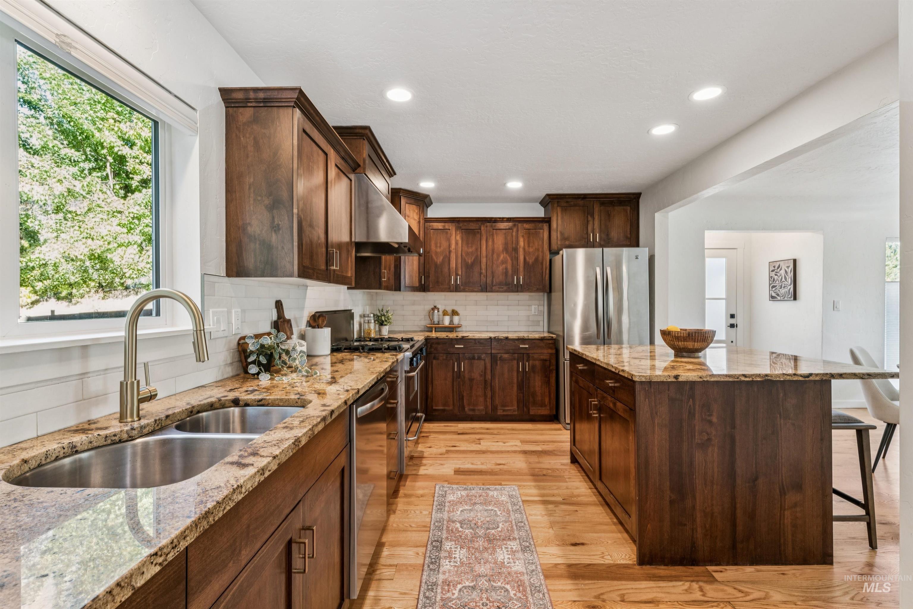 Kitchen with decorative backsplash, a center island, dark brown cabinets, light wood finished floors, and light stone countertops