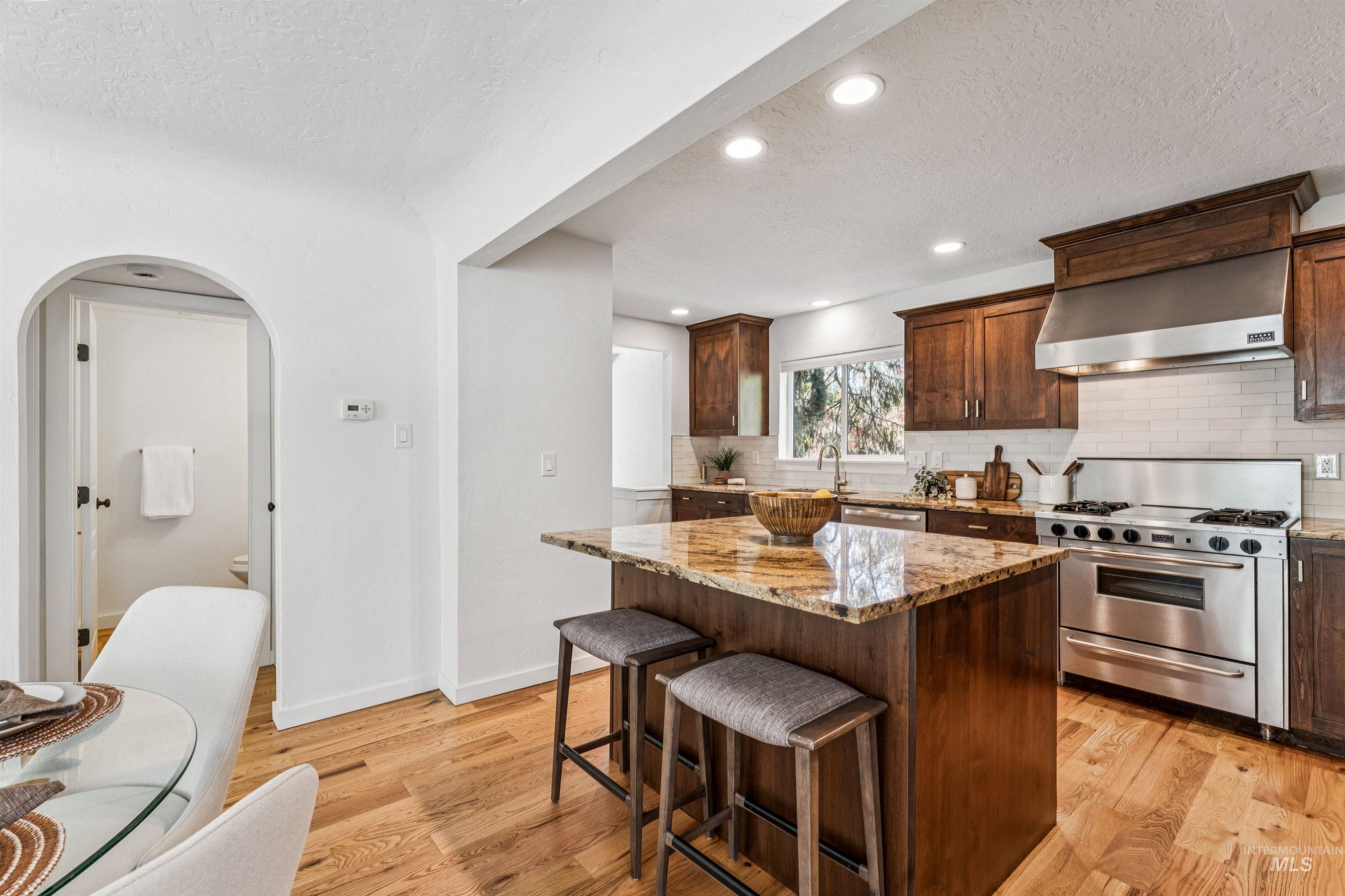 Kitchen with a textured ceiling, arched walkways, decorative backsplash, light wood-style flooring, and appliances with stainless steel finishes