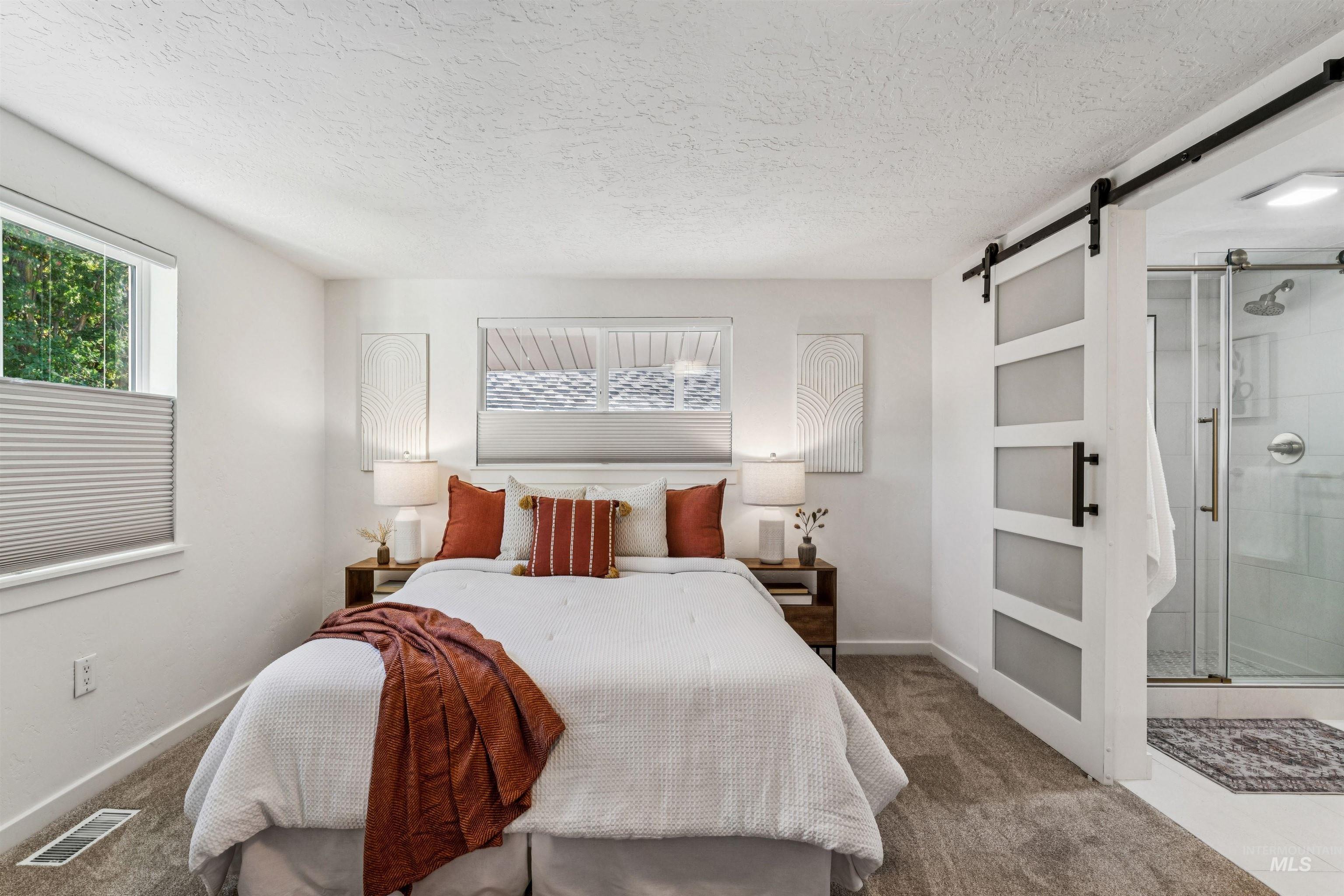 Carpeted primary suite with a barn door and a textured ceiling