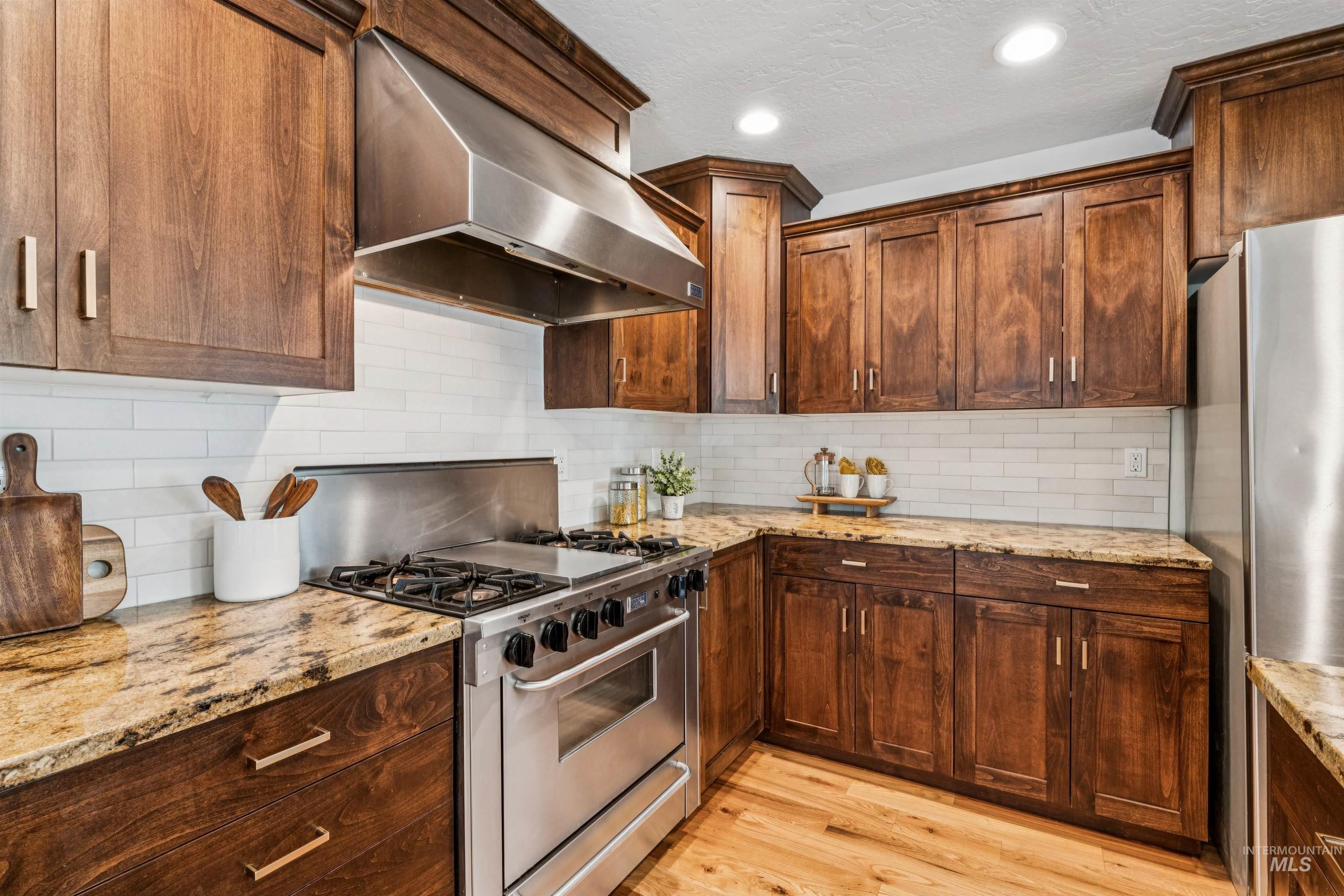 Kitchen featuring ventilation hood, appliances with stainless steel finishes, tasteful backsplash, light wood finished floors, and light stone countertops