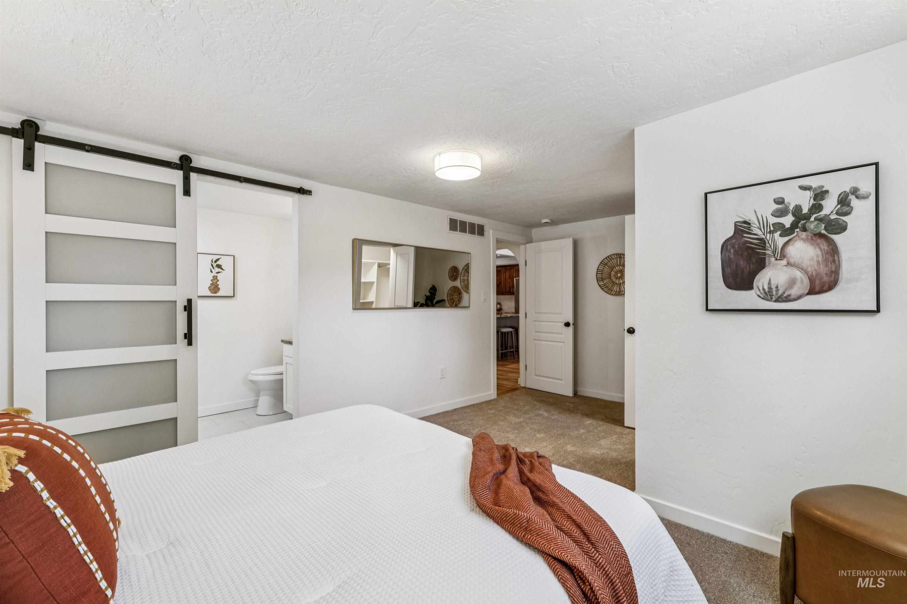 Bedroom with carpet floors, a barn door, a textured ceiling, and connected bathroom