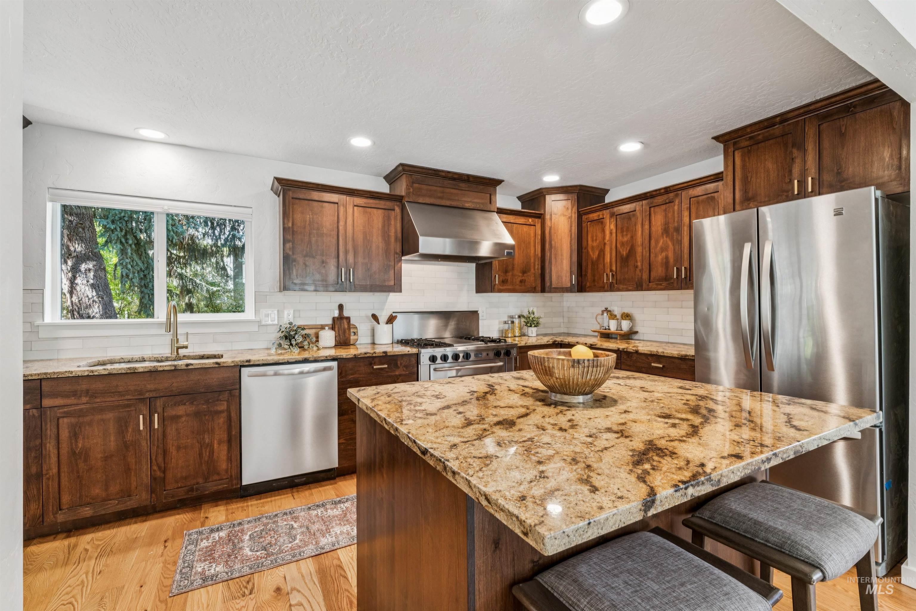 Kitchen featuring a breakfast bar, light wood-type flooring, appliances with stainless steel finishes, wall chimney range hood, and decorative backsplash