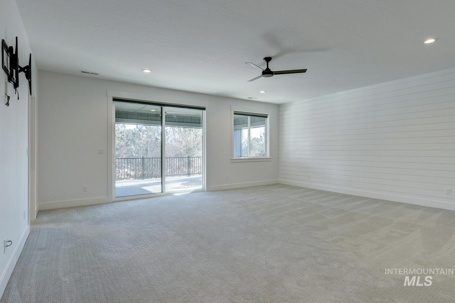 Empty room featuring carpet flooring, wooden walls, and a ceiling fan