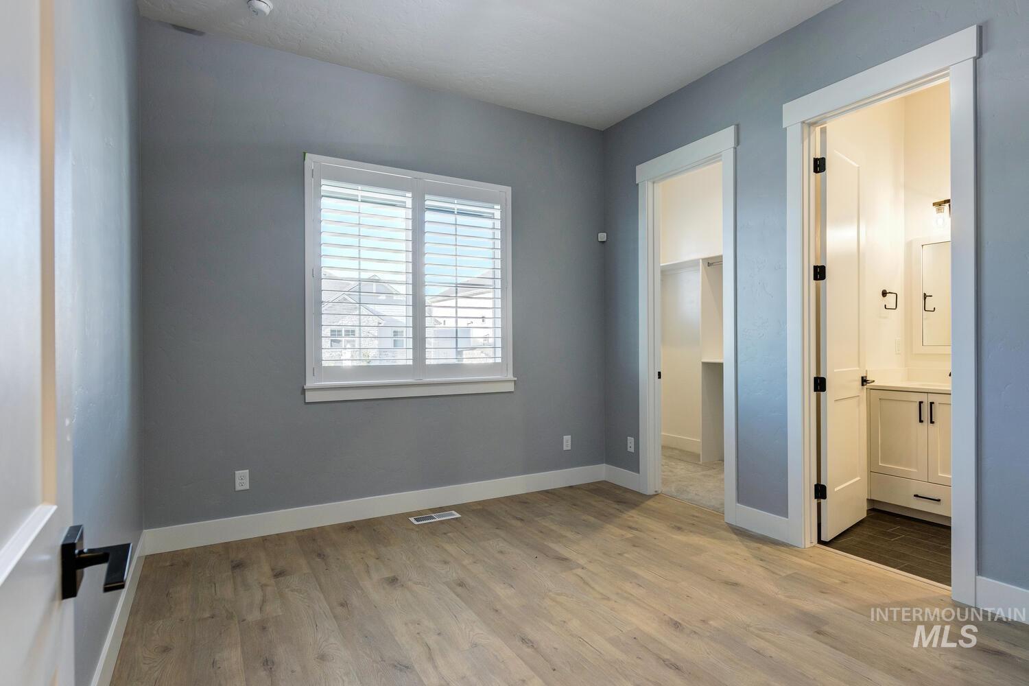 Unfurnished bedroom featuring a walk in closet, light wood finished floors, and ensuite bath