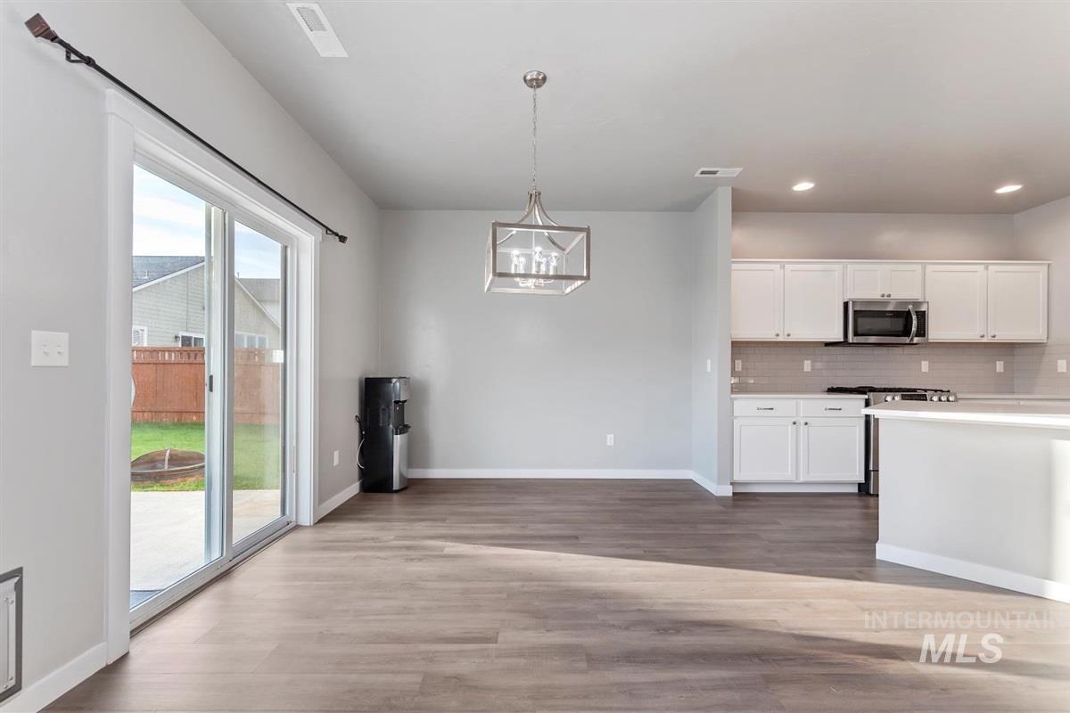 Kitchen with a chandelier, light countertops, white cabinets, tasteful backsplash, and hanging light fixtures