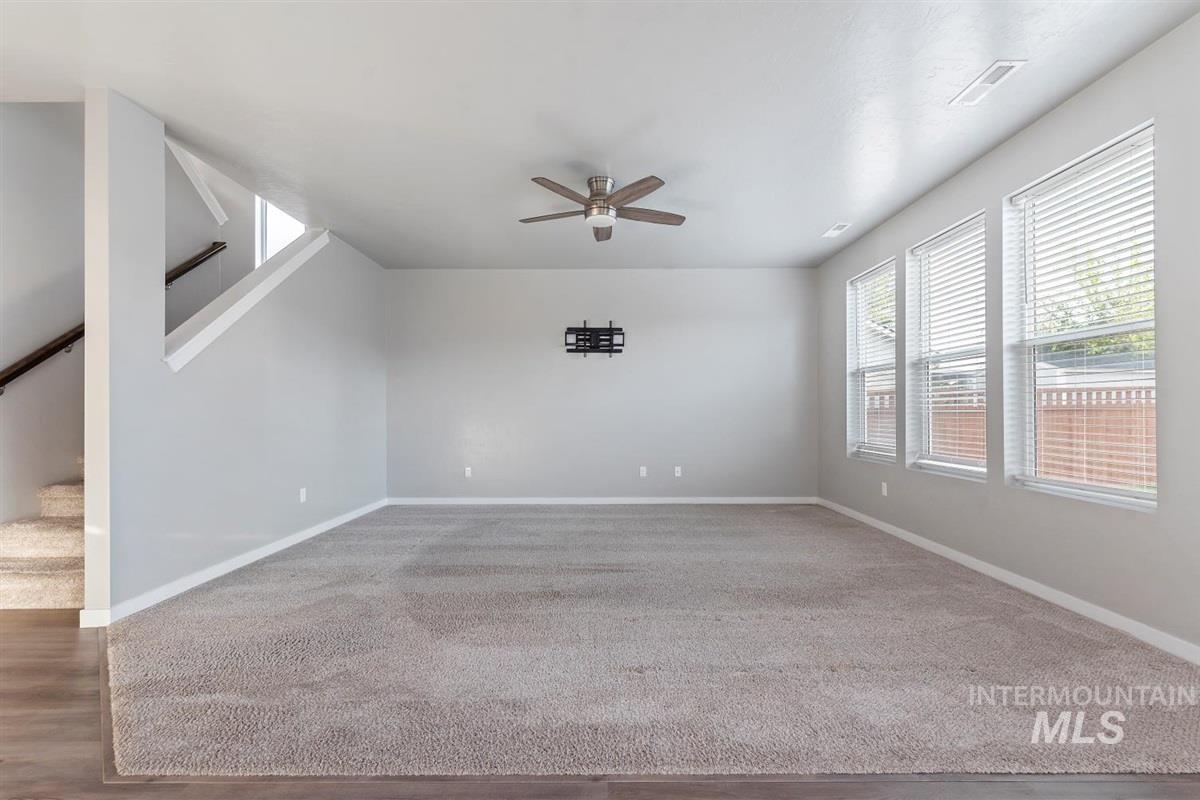 Unfurnished living room with stairs, ceiling fan, and carpet floors