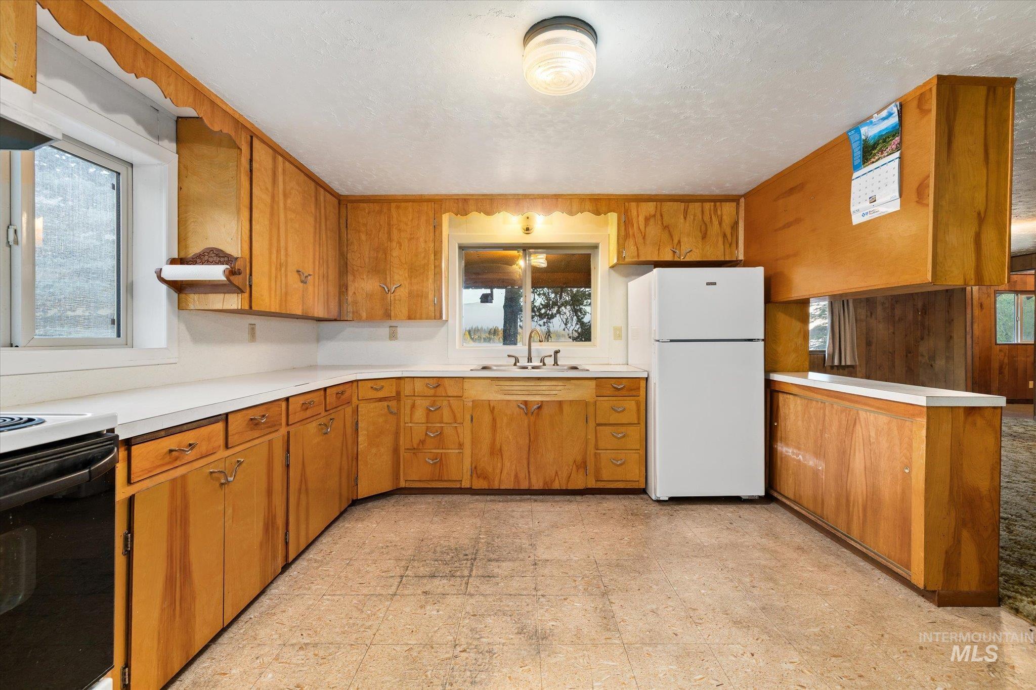 Kitchen featuring extensive wood cabinetry, white countertops, a double-basin sink, and tile-finish flooring