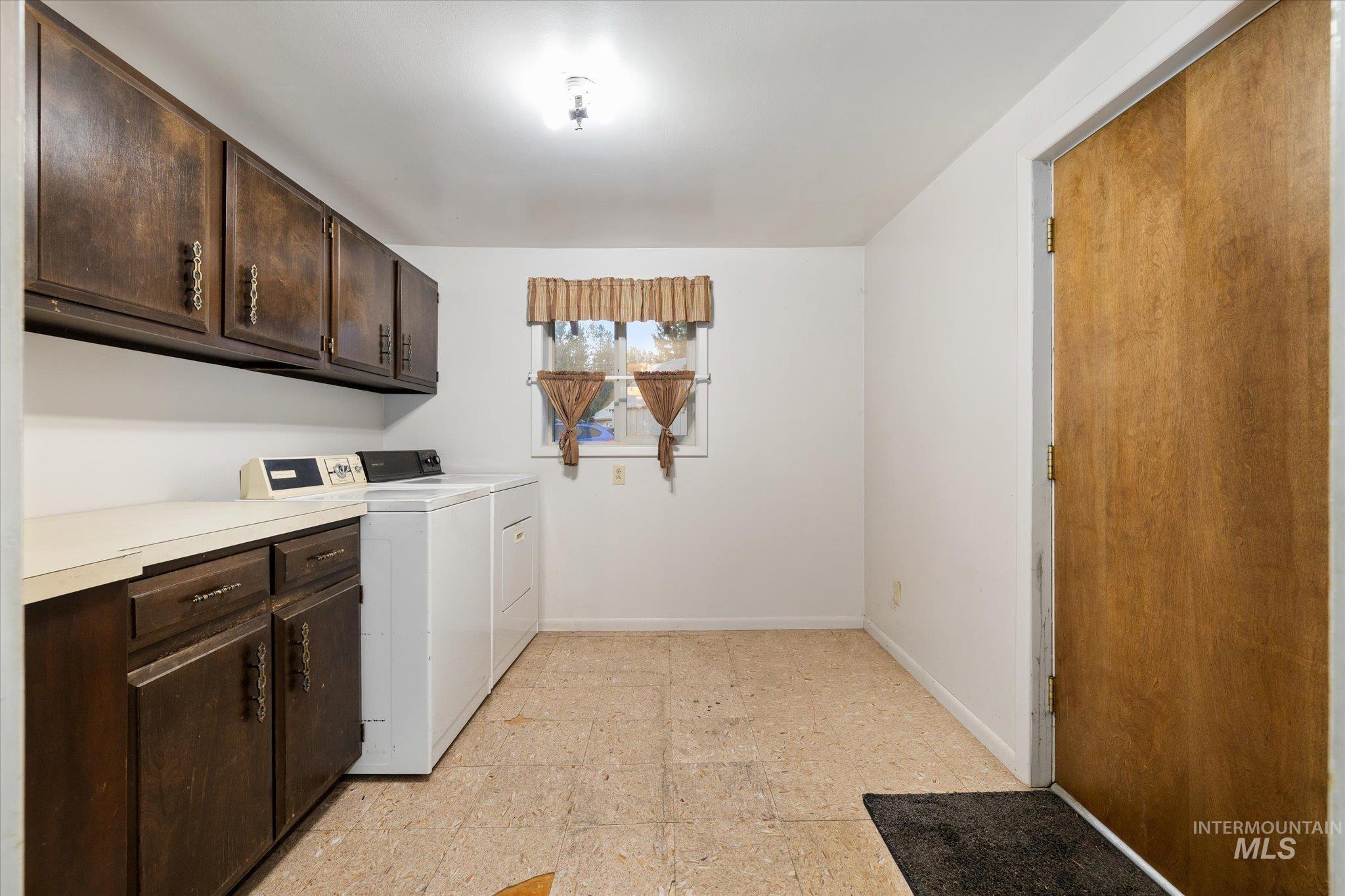 Utility room with white walls, wood-finish cabinetry, a light-toned countertop, and a window providing natural illumination