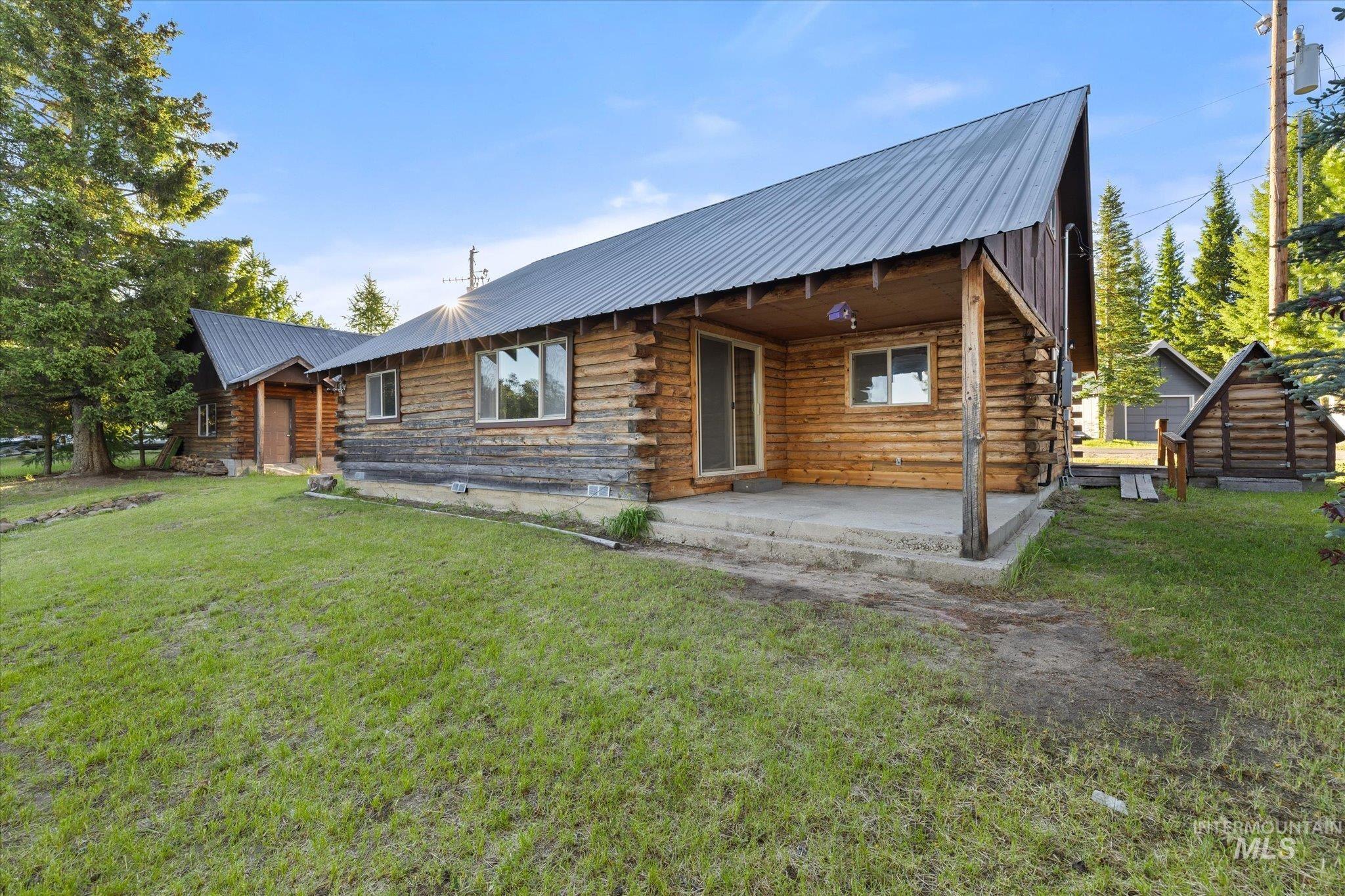 Rustic log cabin exterior with a metal roof and a covered concrete patio