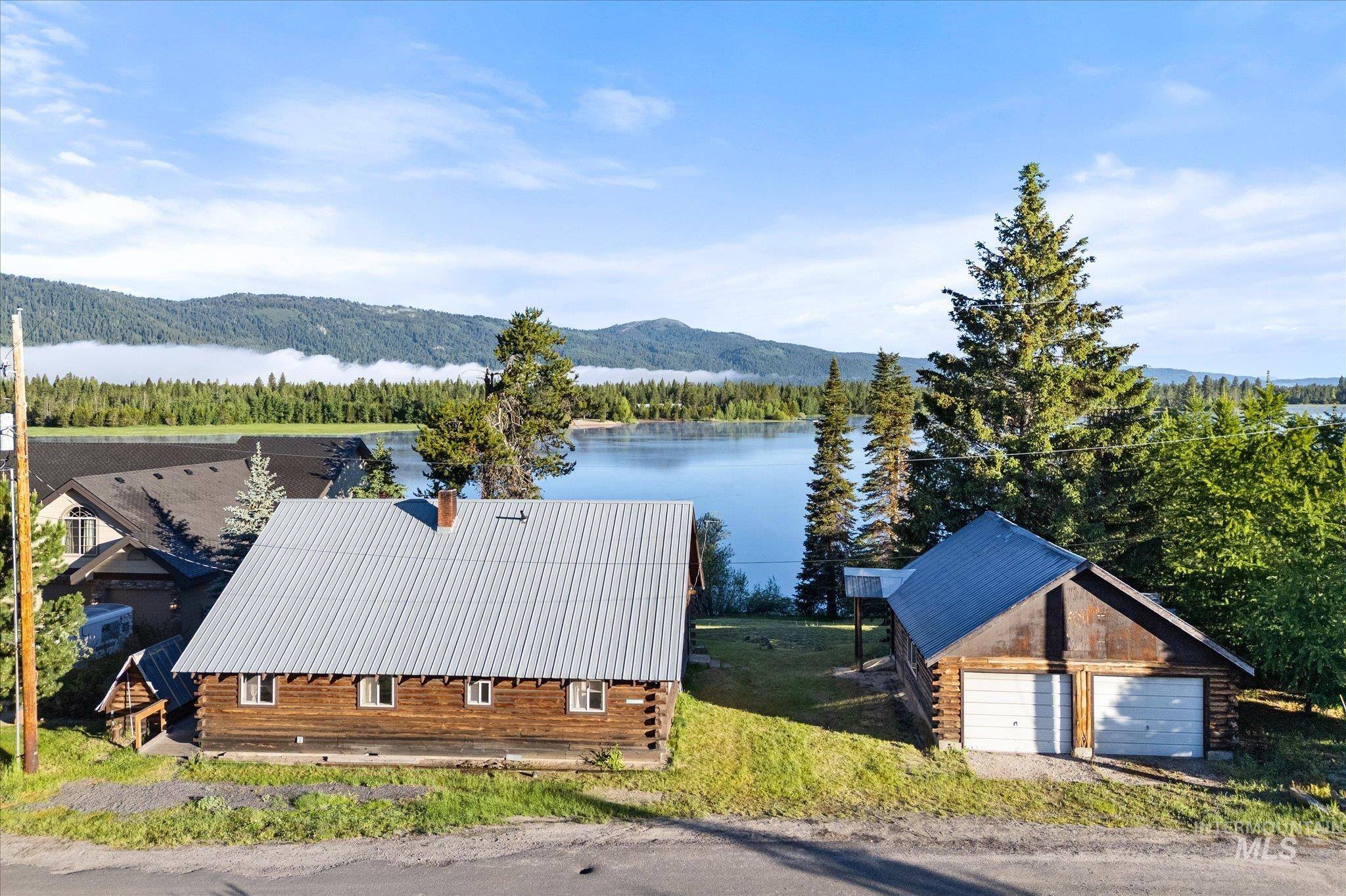 Waterfront property featuring a log cabin exterior, metal roof, detached two-car garage, and established trees