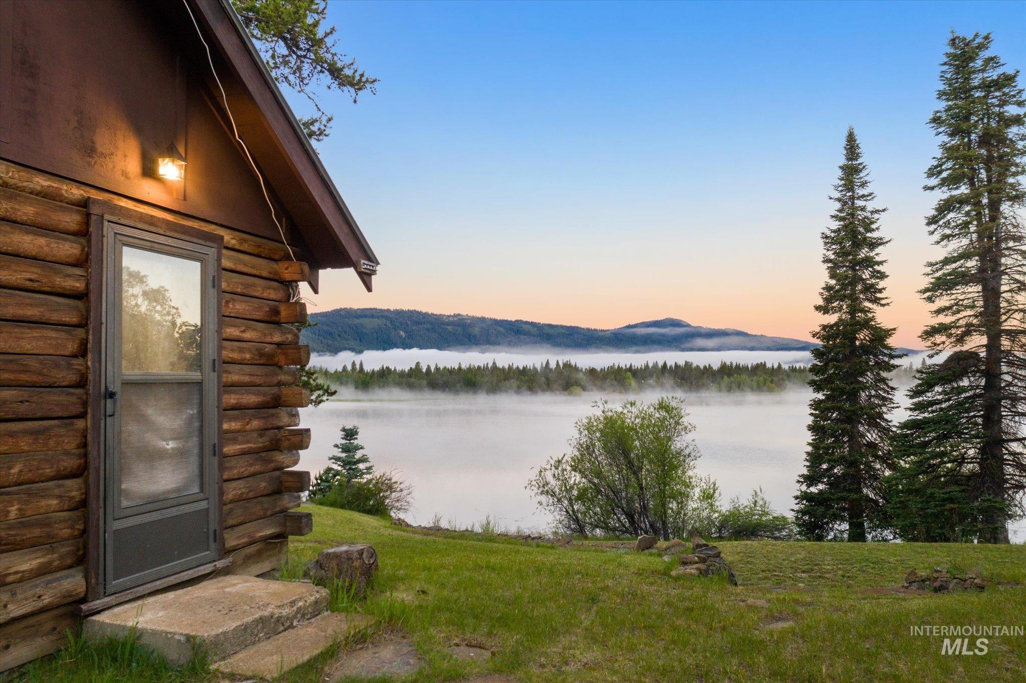 Log cabin exterior with a concrete step entry, overlooking a body of water with distant mountains