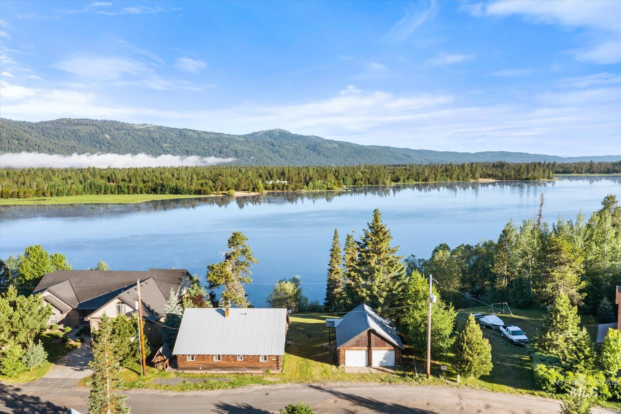 Lakefront property with a rustic cabin, detached two-car garage, and a secondary residence featuring a dark shingle roof