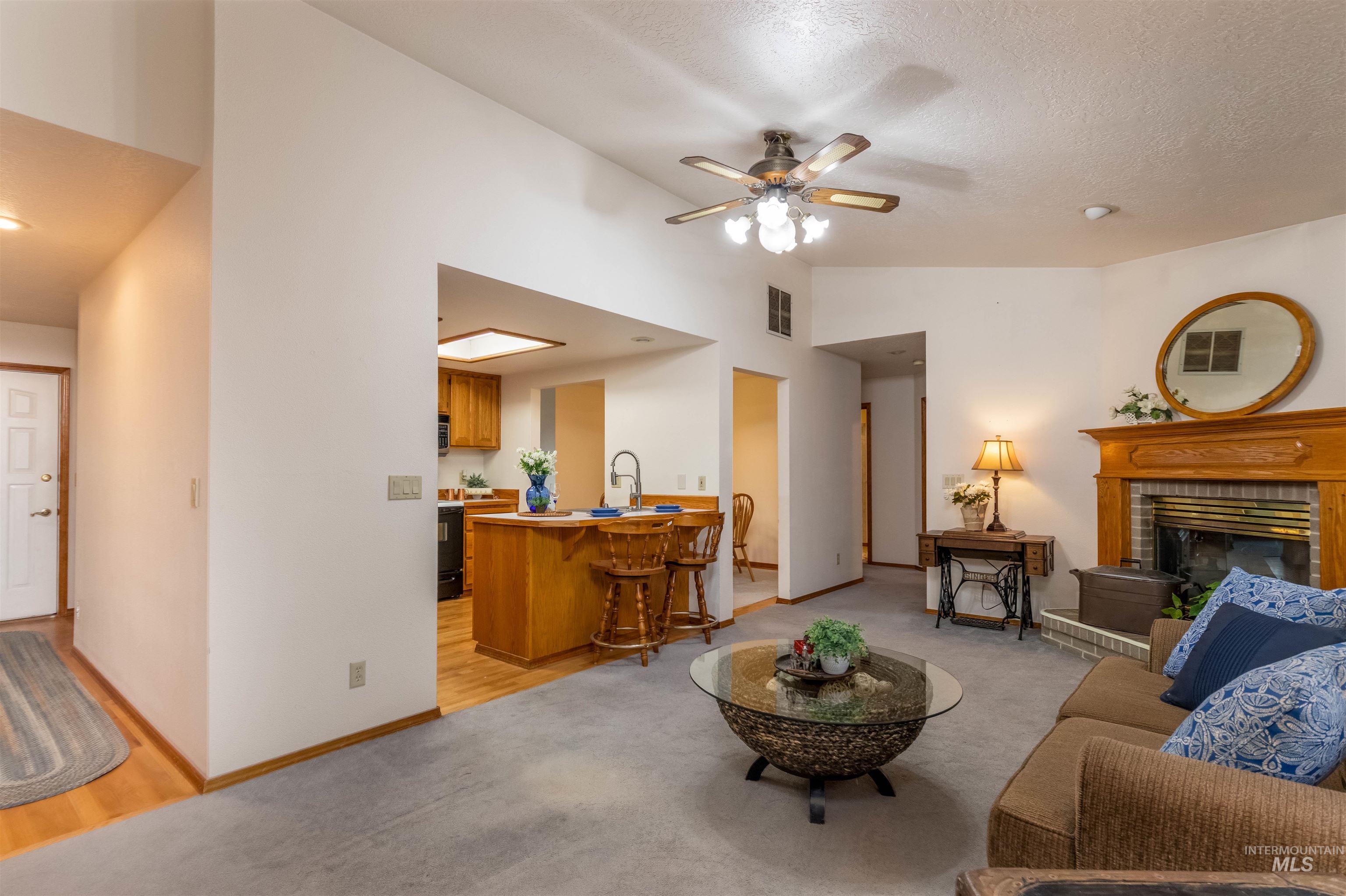 Living room with light colored carpet, lofted ceiling, ceiling fan, a fireplace, and a textured ceiling
