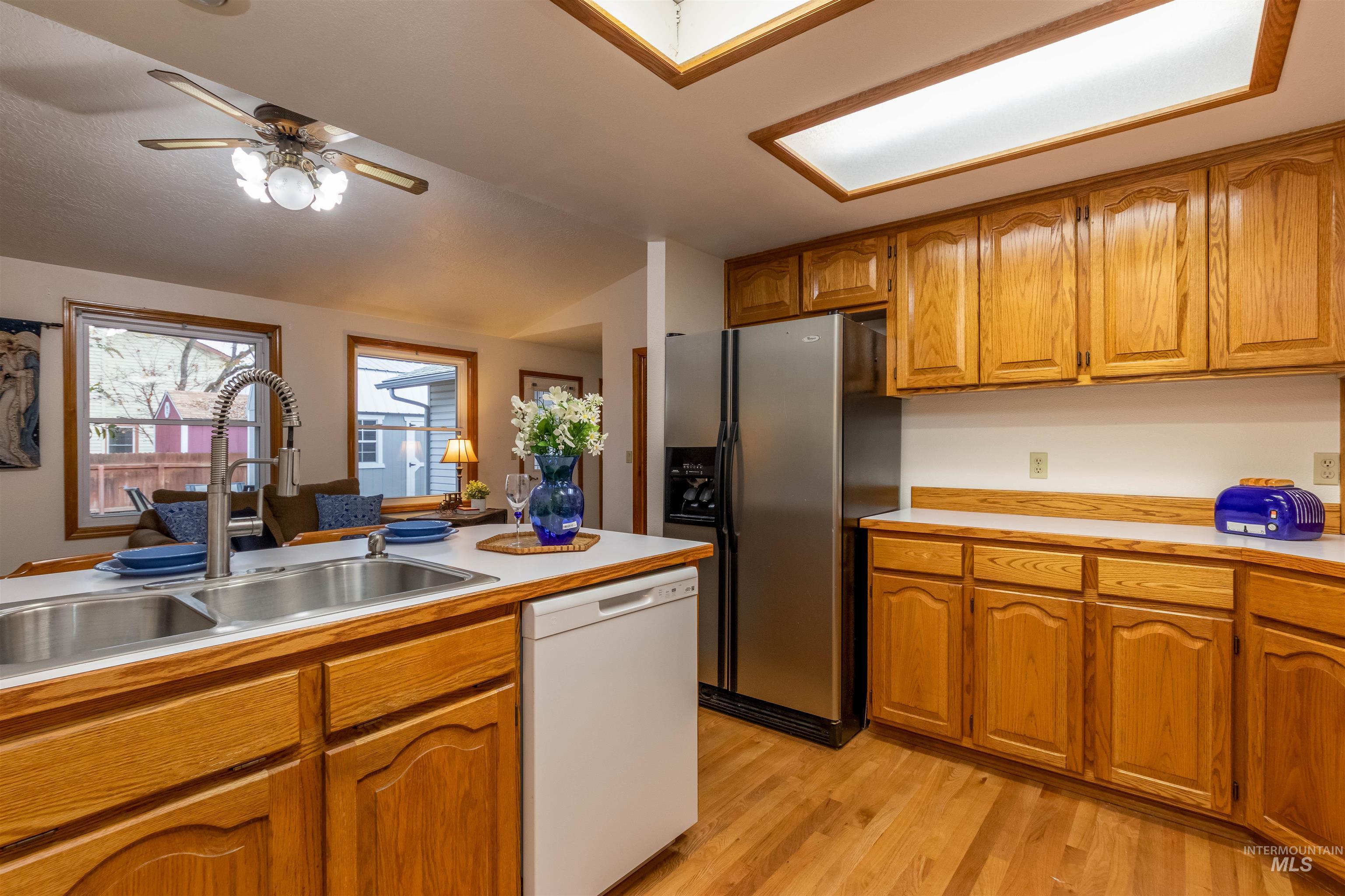 Kitchen featuring brown cabinets, light countertops, dishwasher, stainless steel refrigerator with ice dispenser, and light wood finished floors