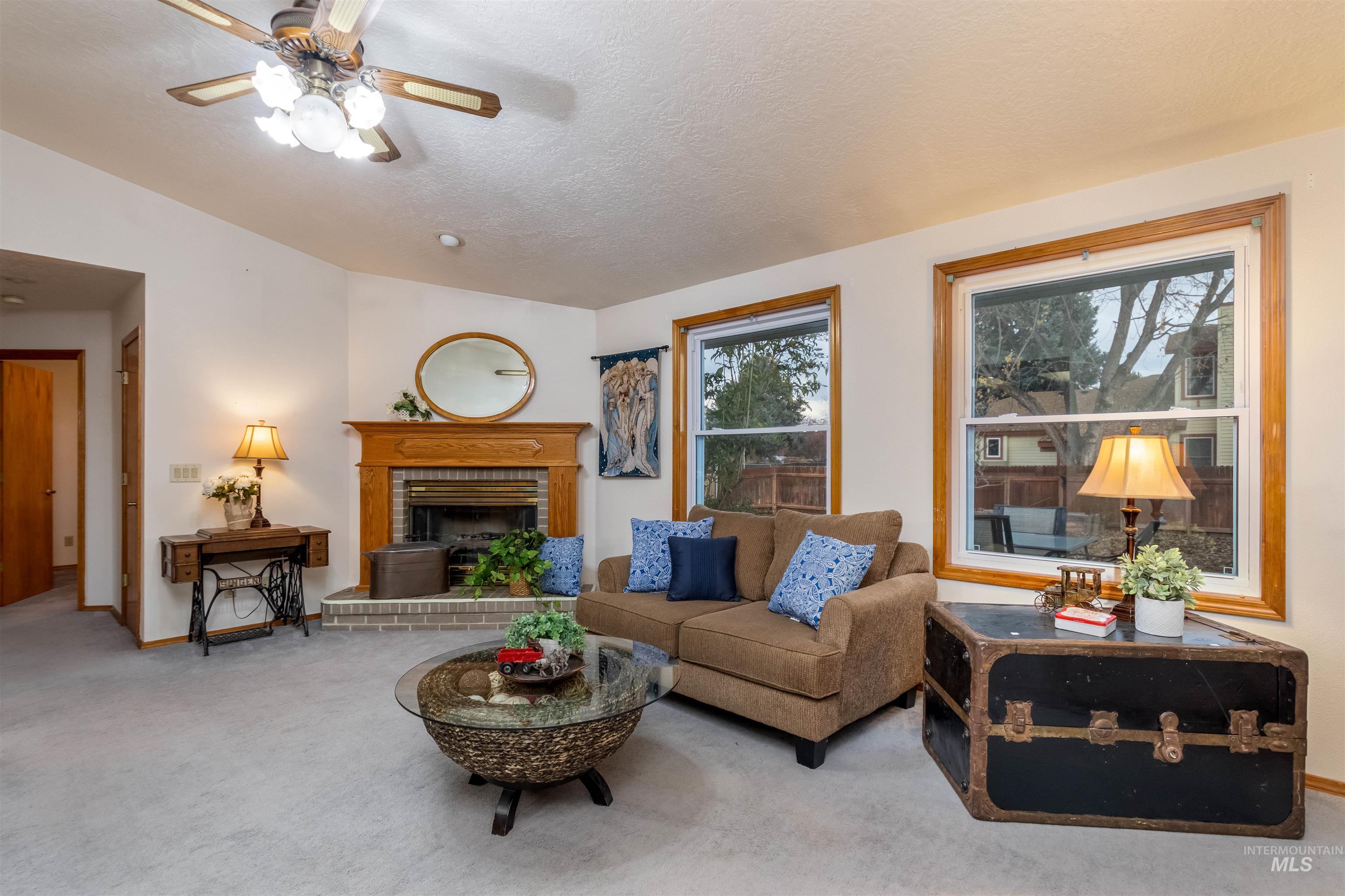 Living room with lofted ceiling, carpet floors, ceiling fan, a brick fireplace, and a textured ceiling