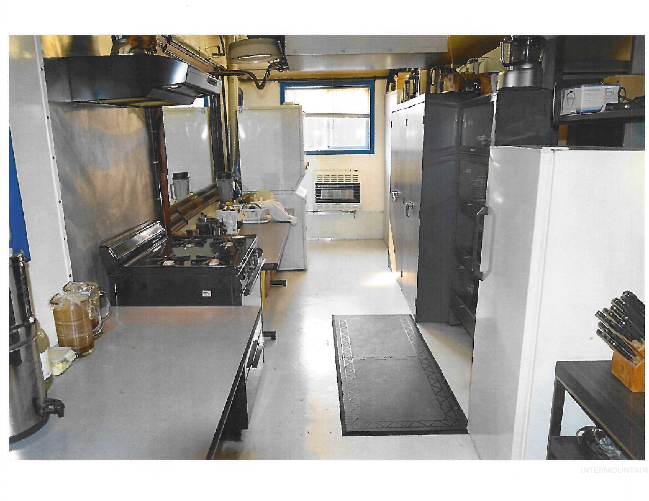 Kitchen featuring freestanding refrigerator, heating unit, under cabinet range hood, and concrete flooring