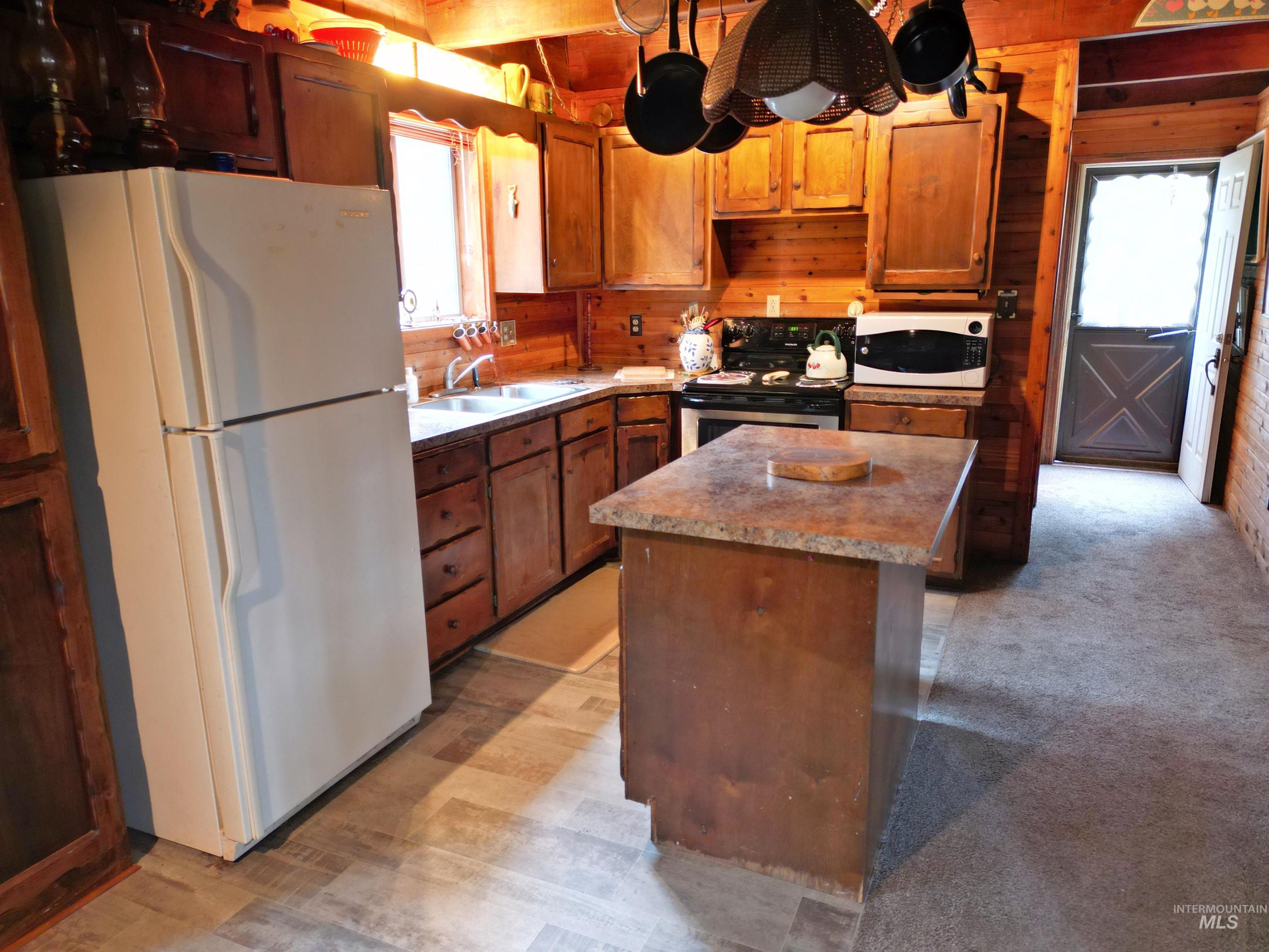 Kitchen with wooden walls, white appliances, a kitchen island, brown cabinetry, and light carpet