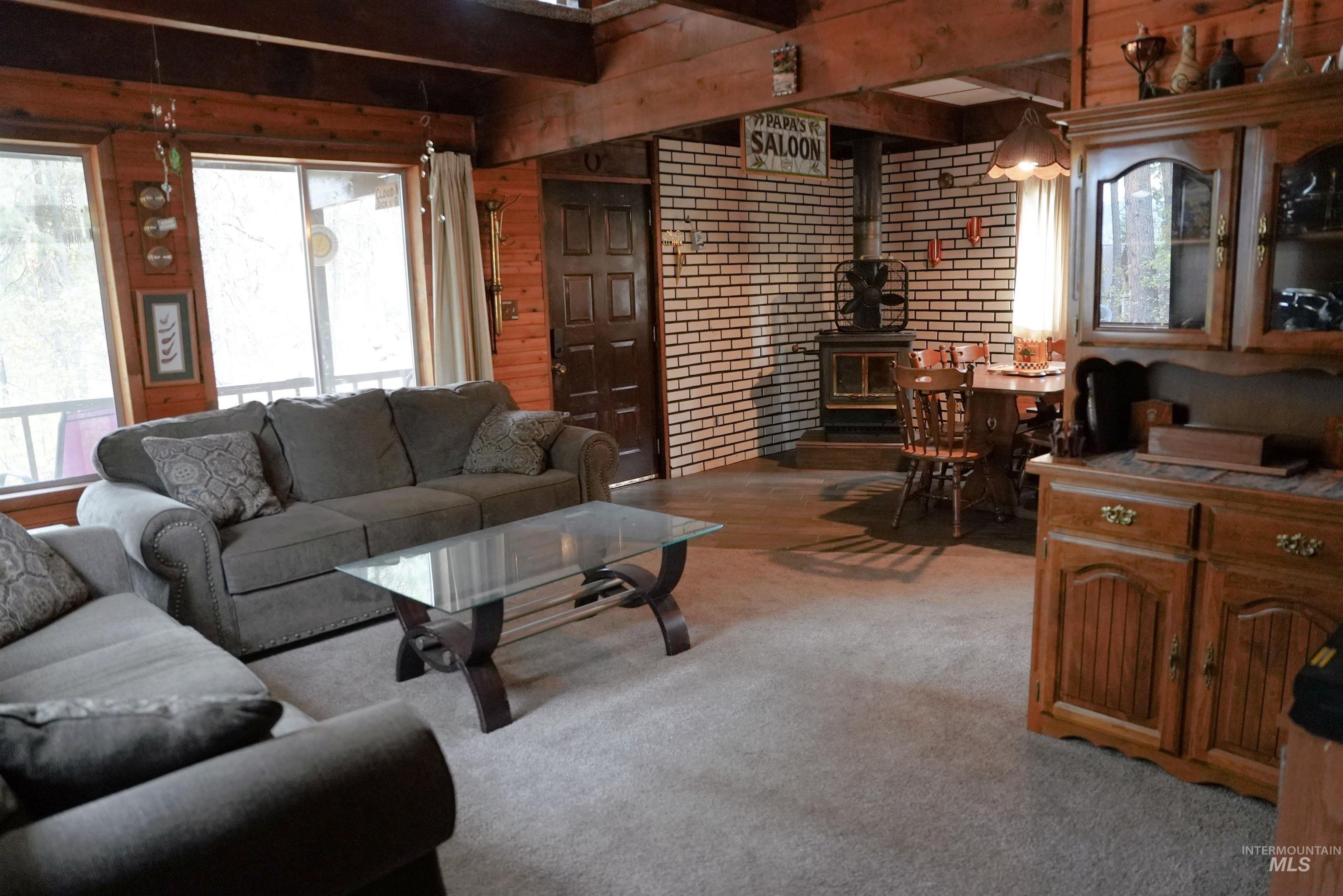 Living area featuring a wood stove, beamed ceiling, light colored carpet, and wood walls
