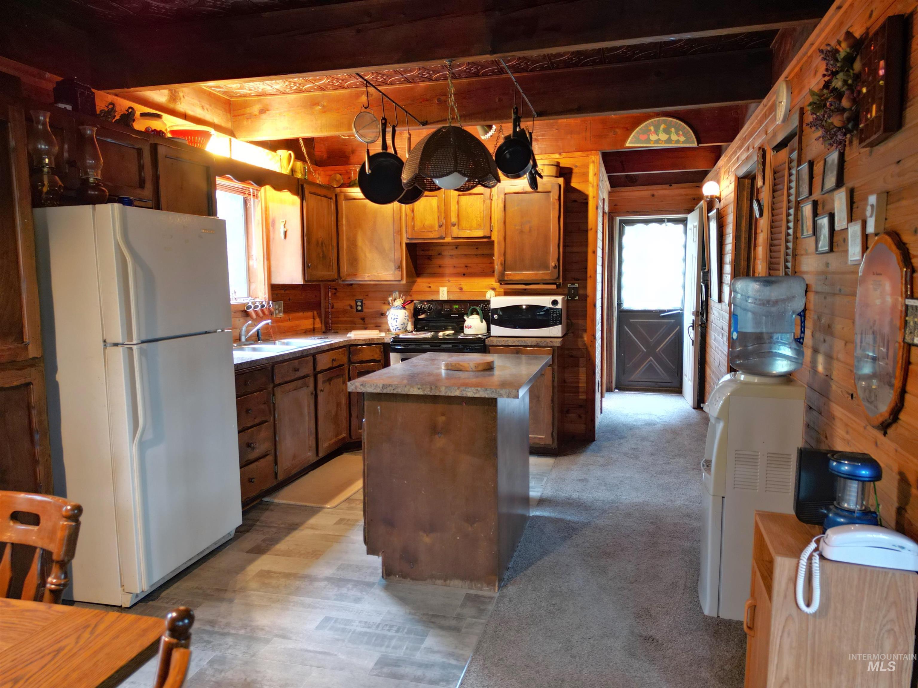 Kitchen featuring white appliances, a center island, beam ceiling, wood walls, and light carpet
