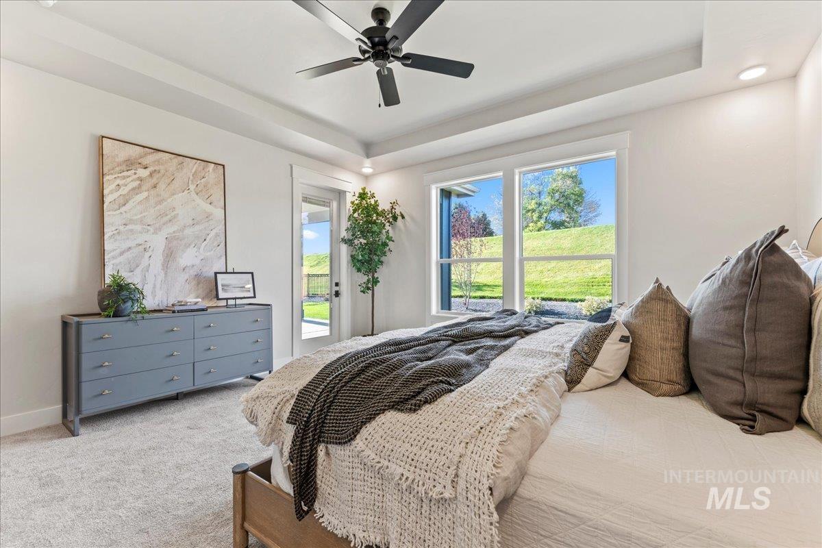 Bedroom with light carpet, a tray ceiling, multiple windows, and access to outside