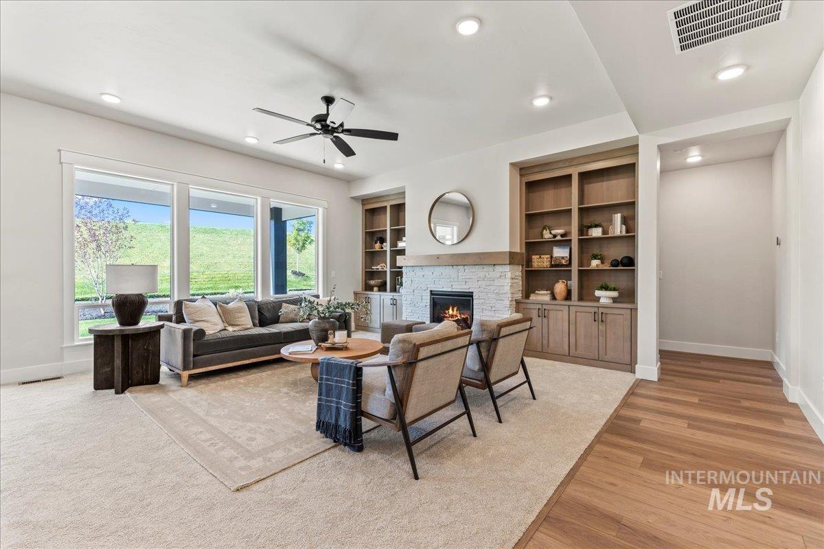 Living area featuring a stone fireplace, recessed lighting, ceiling fan, light wood-style flooring, and built in features