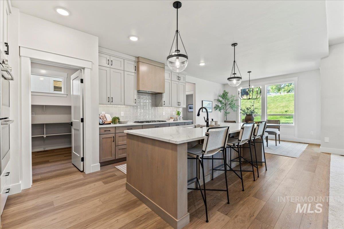 Kitchen with brown cabinets, a kitchen breakfast bar, tasteful backsplash, hanging light fixtures, and light wood-type flooring