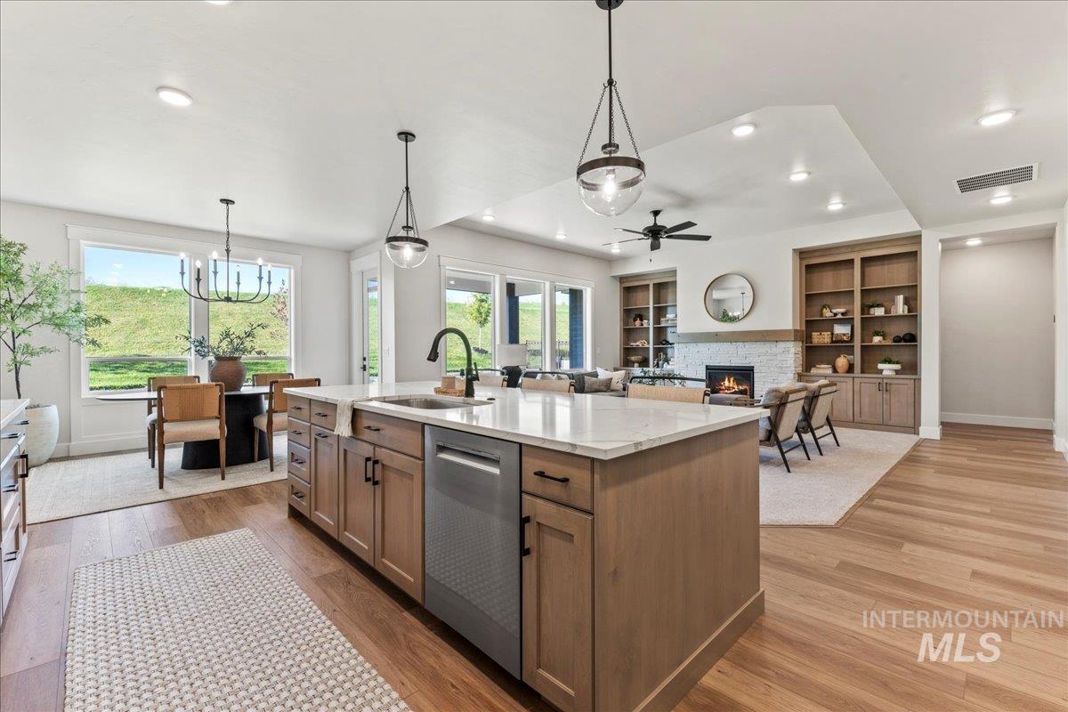 Kitchen featuring hanging light fixtures, a stone fireplace, light wood finished floors, dishwasher, and light stone countertops