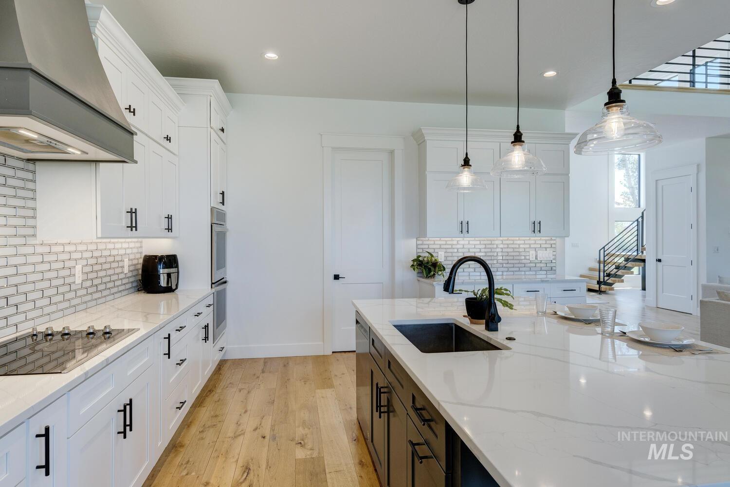 Kitchen with premium range hood, black electric stovetop, white cabinets, decorative backsplash, and healthy amount of natural light
