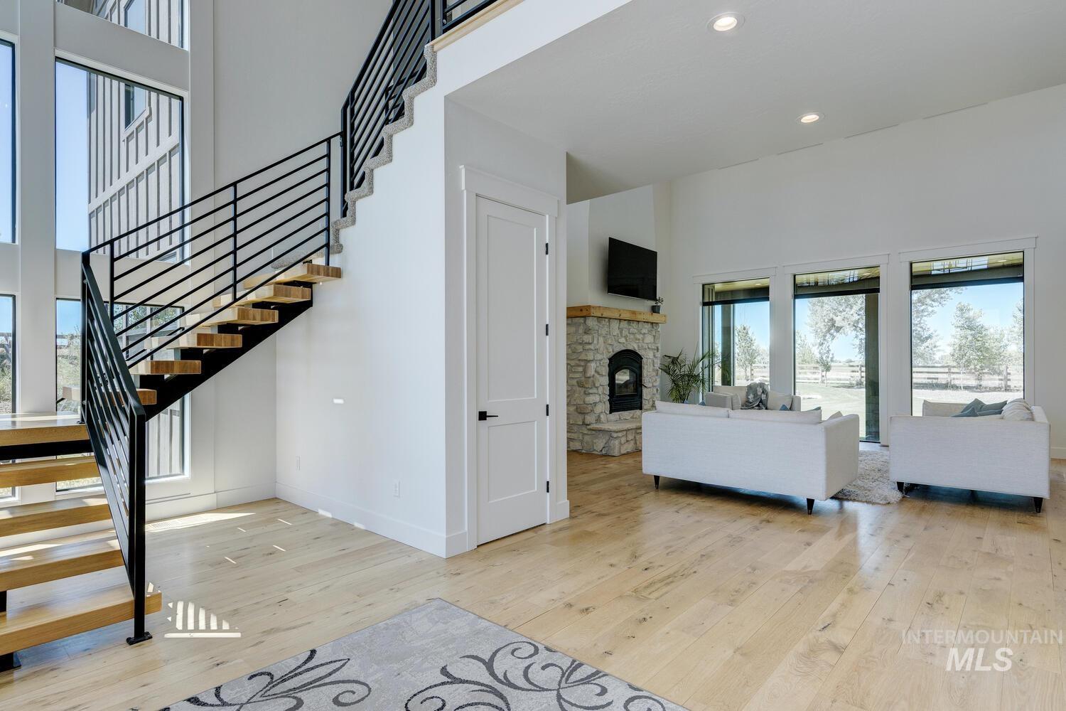 Living area featuring hardwood / wood-style flooring, stairway, a high ceiling, a stone fireplace, and recessed lighting