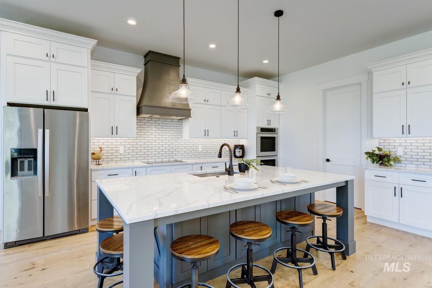 Kitchen featuring stainless steel appliances, premium range hood, light wood finished floors, white cabinetry, and recessed lighting