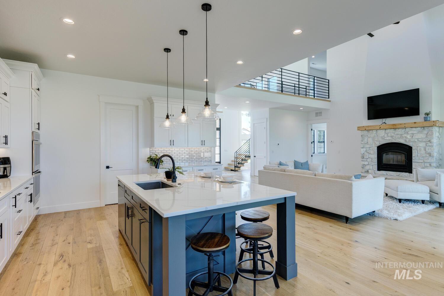 Kitchen featuring light wood-style floors, white cabinets, light stone countertops, an island with sink, and open floor plan