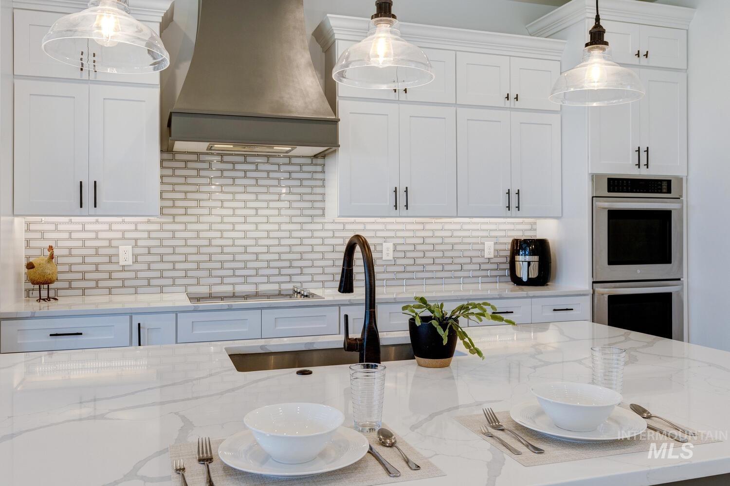 Kitchen with premium range hood, stainless steel double oven, cooktop, tasteful backsplash, and white cabinetry